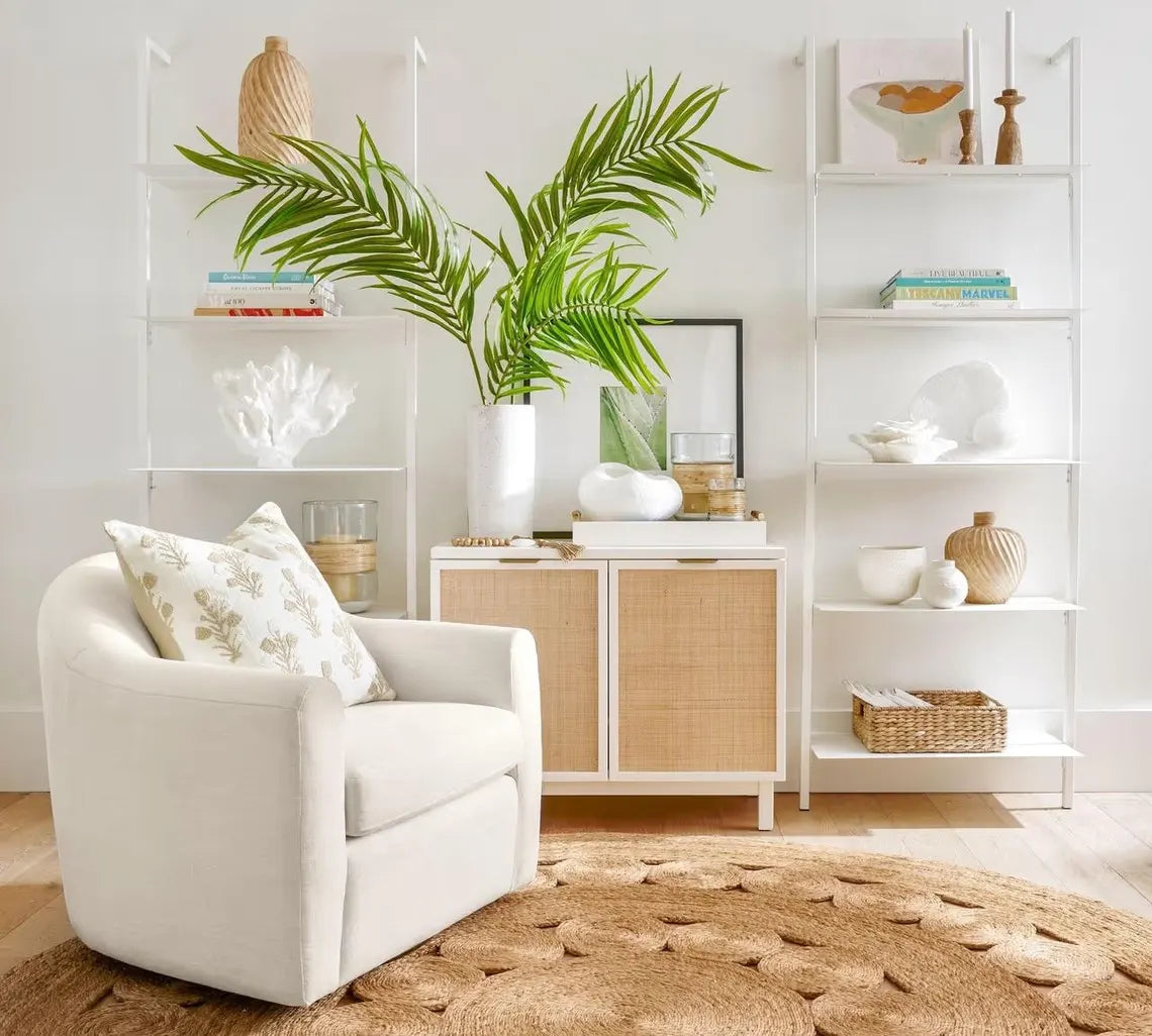 Bask Jute Rug styled in a bright living room with a white armchair, neutral decor, and green indoor plants, highlighting the rug’s natural round design and earthy tone.