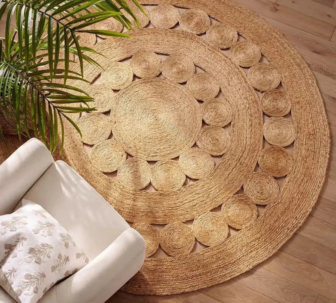 Round Bask Jute Rug styled in a cozy living room with a white sofa and indoor plant, highlighting its circular braided pattern and natural golden hue.