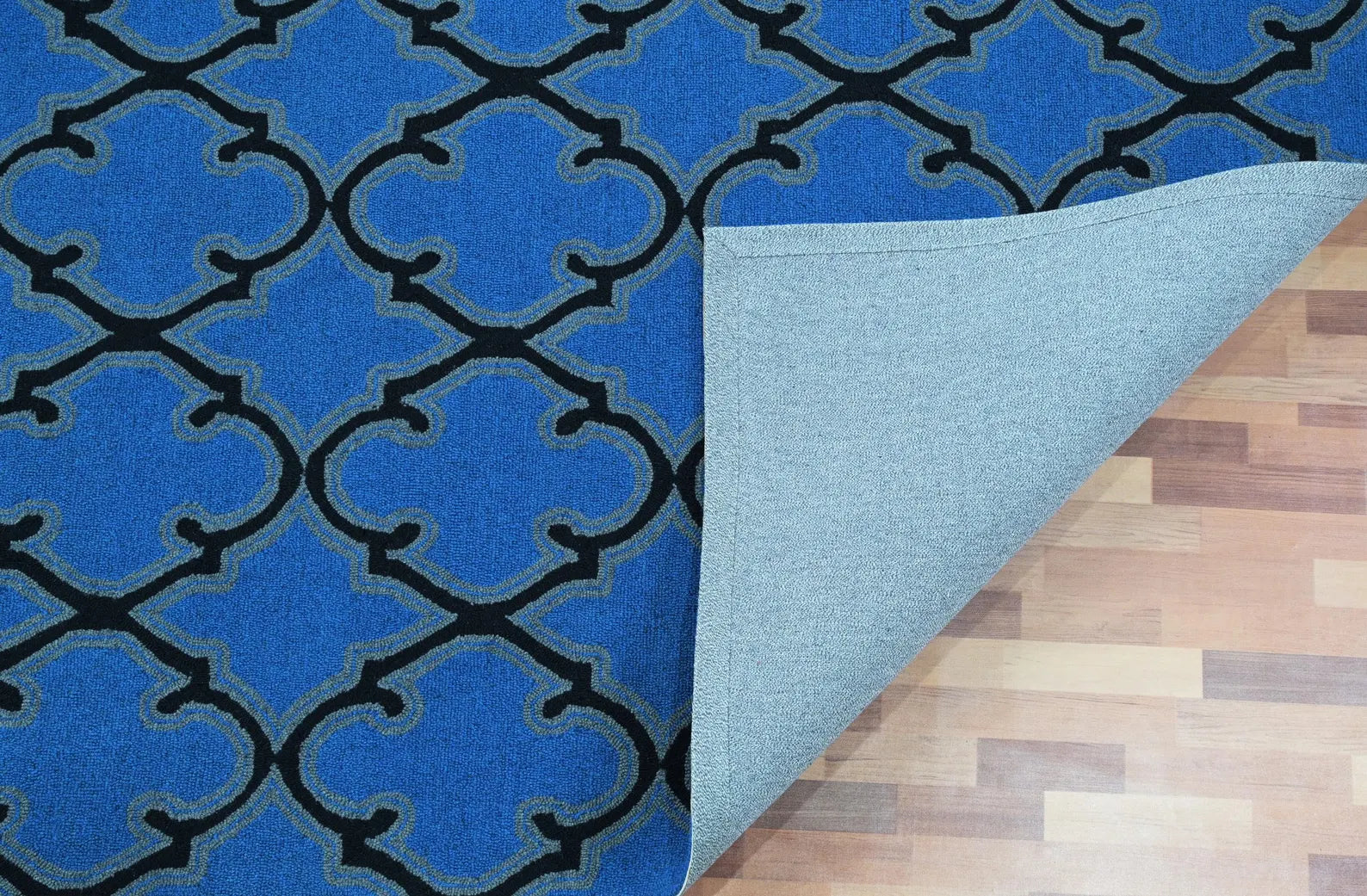 Bluenox Rug corner view showing deep blue geometric pattern with black trellis detailing and visible backing on wooden floor.