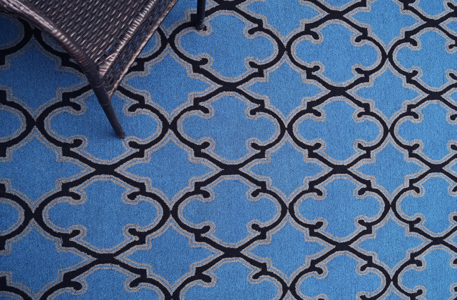 Folded edge close-up of Bluenox Rug displaying soft wool texture, black trellis design, and detailed craftsmanship on deep blue surface.