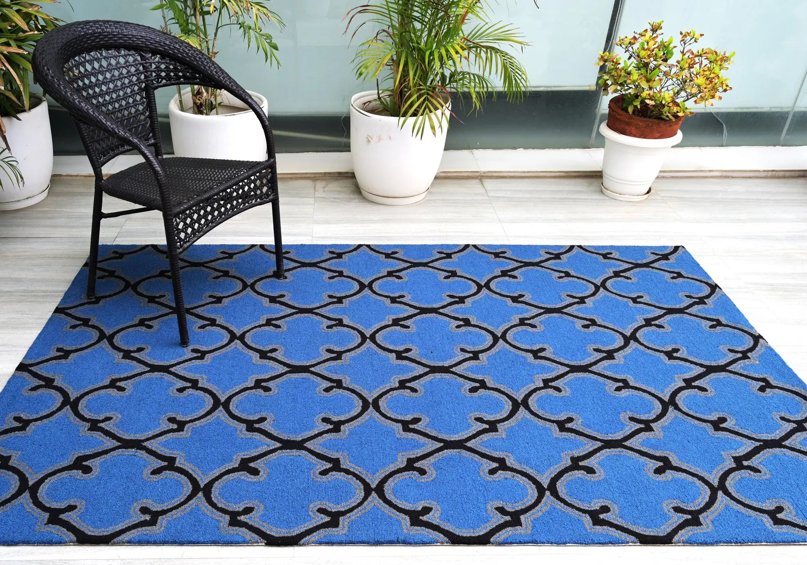 Bluenox Rug styled in a modern open space with a wooden chair and green plants, showcasing its deep blue tone and black geometric pattern in natural daylight.