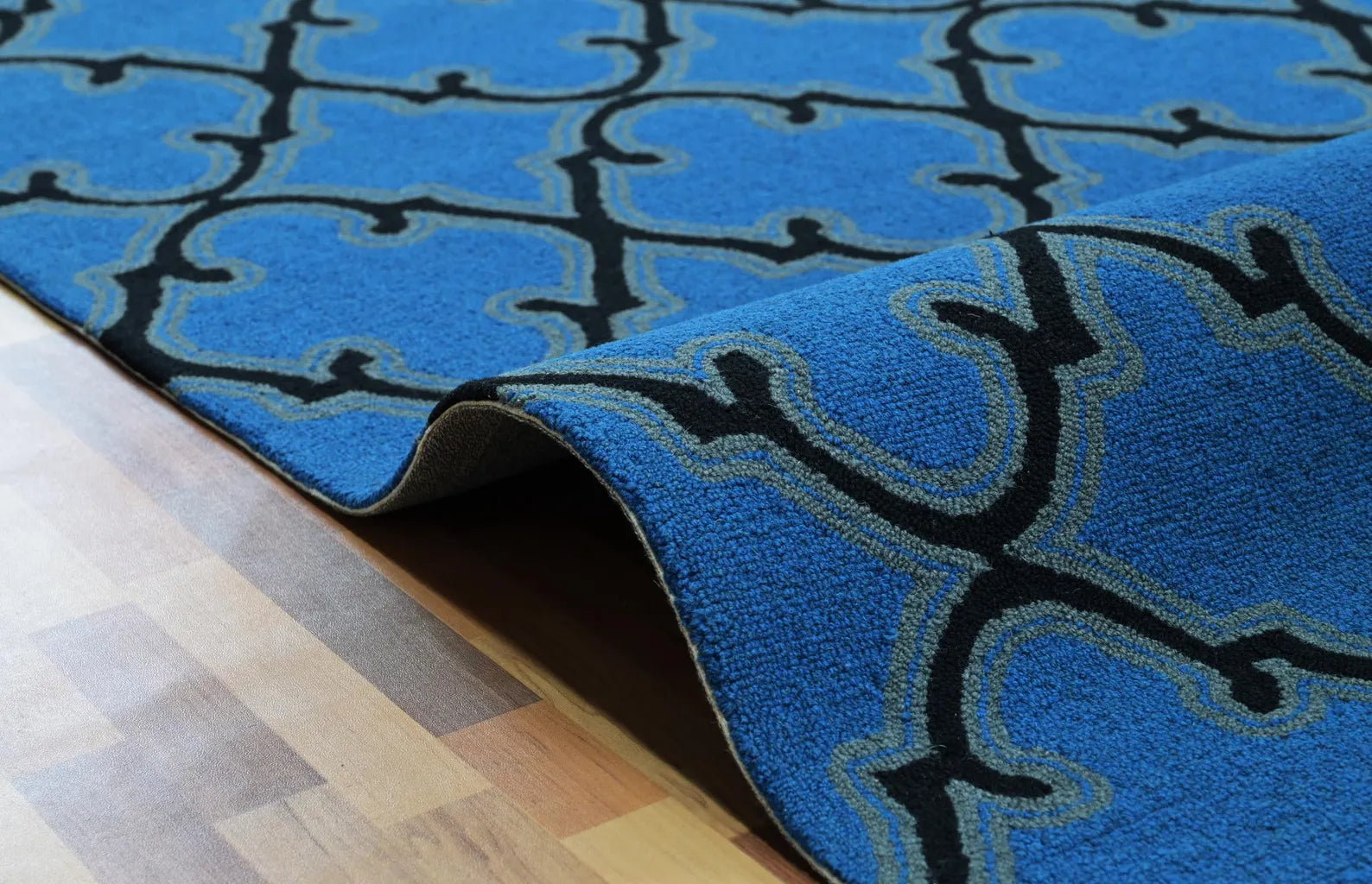 Waved close-up of Bluenox hand tufted rug showing soft hand-tufted wool surface, deep blue hue, and black trellis geometric lines curving naturally over the floor.
