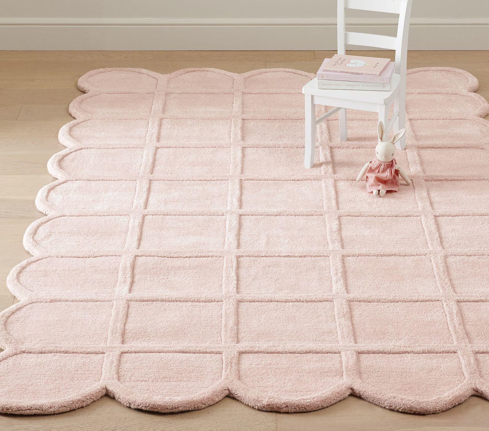 Blush Quilt Rug styled in a pastel room with a white chair on top, showcasing its soft pink tone and scalloped quilted edges.