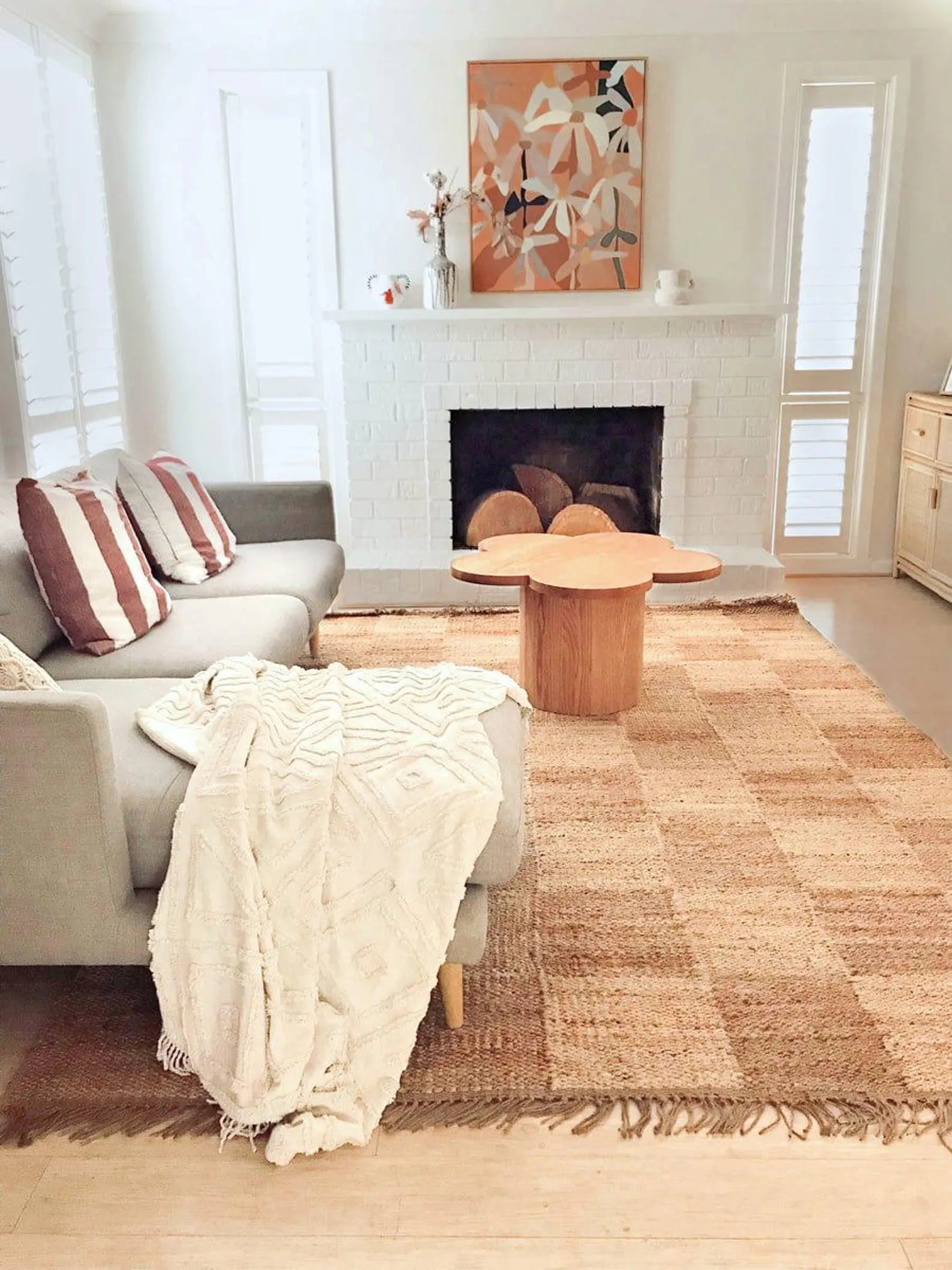 Chesson Rug placed in a cozy modern living room with a grey sofa, wooden coffee table, and warm sunlight highlighting its beige and brown checker pattern with fringed edges.
