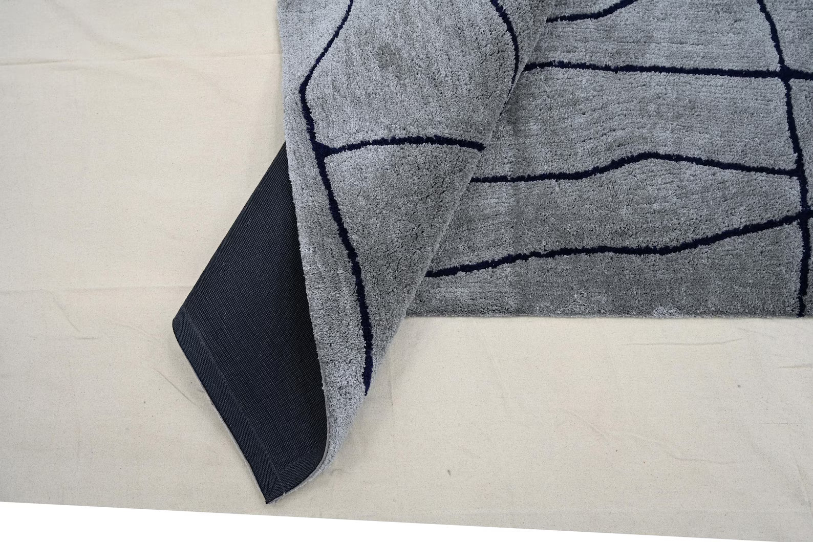 Corner fold detail view of Abstract Line Art Grey Rug showing grey textured surface with dark abstract lines and durable woven backing
