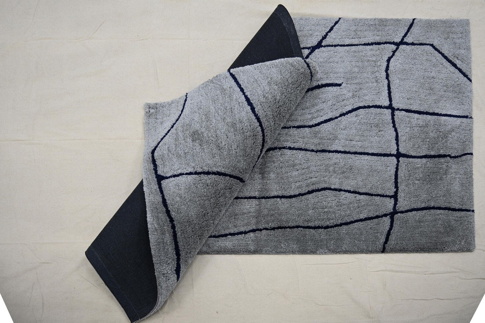 Corner fold top angle view of Abstract Line Art Grey Rug showing grey surface with dark abstract lines and soft flexible backing