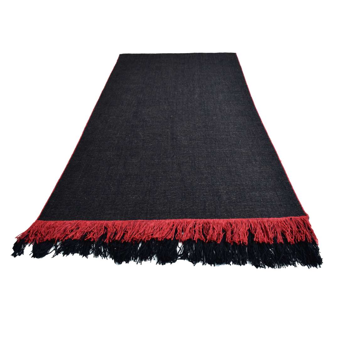 Full view of Auskin Luxury Black Rug displayed flat with red tasseled edges and solid black wool texture in neutral lighting