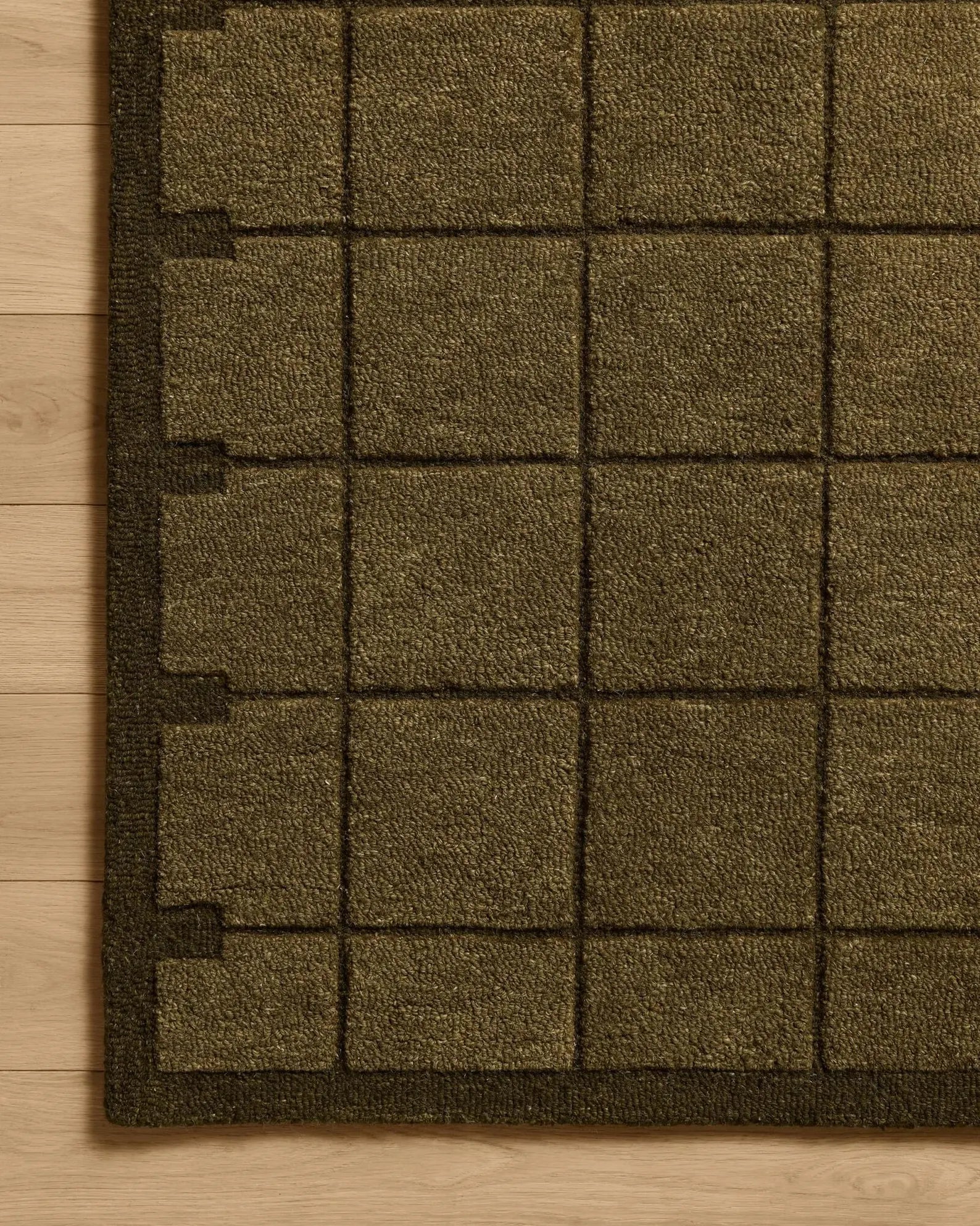 Hand tufted Gridform rug corner closeup showing the olive grid pattern on a wooden floor.