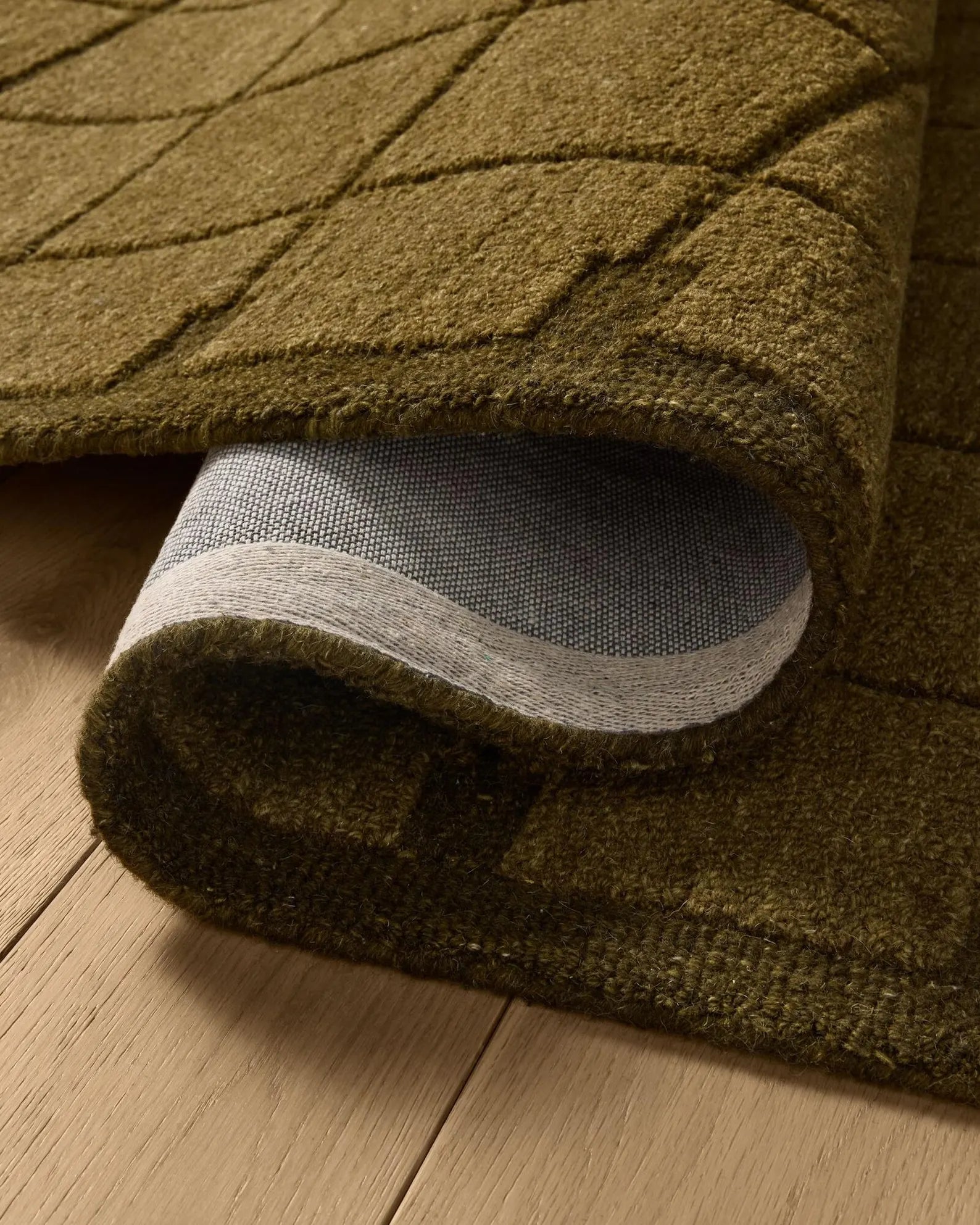 Hand tufted Gridform rug rolled edge detail showing the olive grid pattern and backing on a wooden floor.