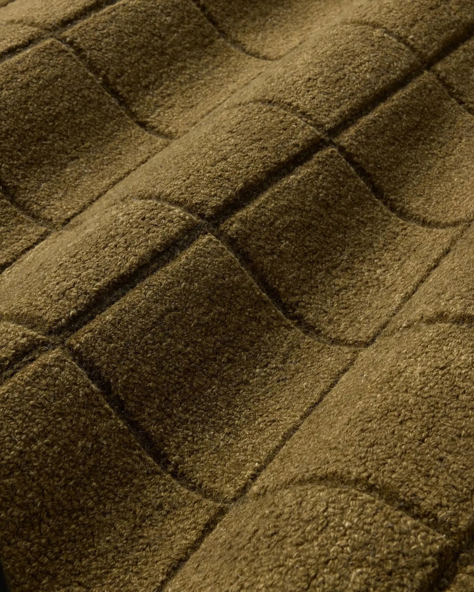 Hand tufted Gridform rug texture closeup showing the raised olive grid pattern in soft lighting.