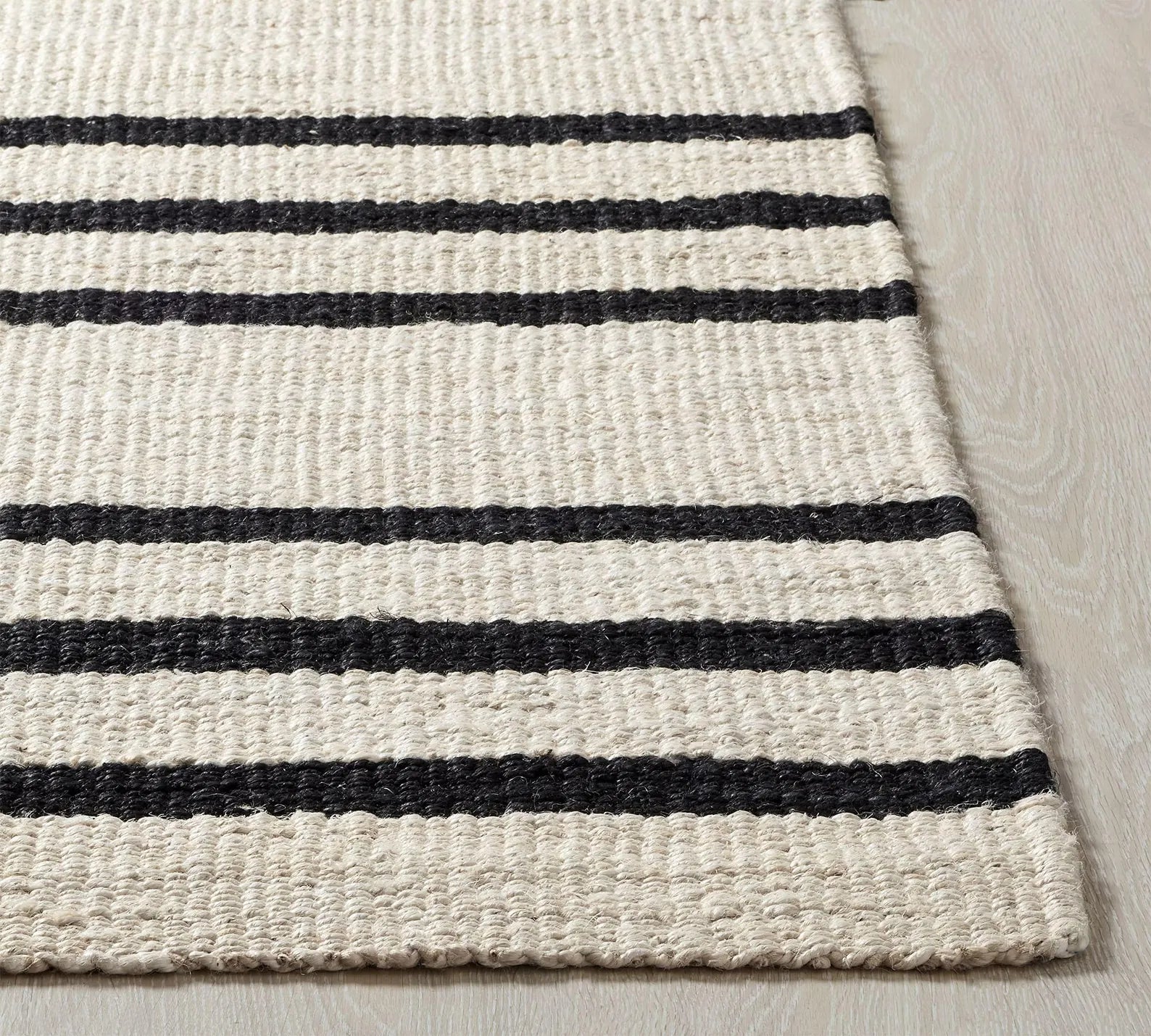 Loomtrail Rug corner detail showing bold black stripes on ivory base placed over a light wooden floor.