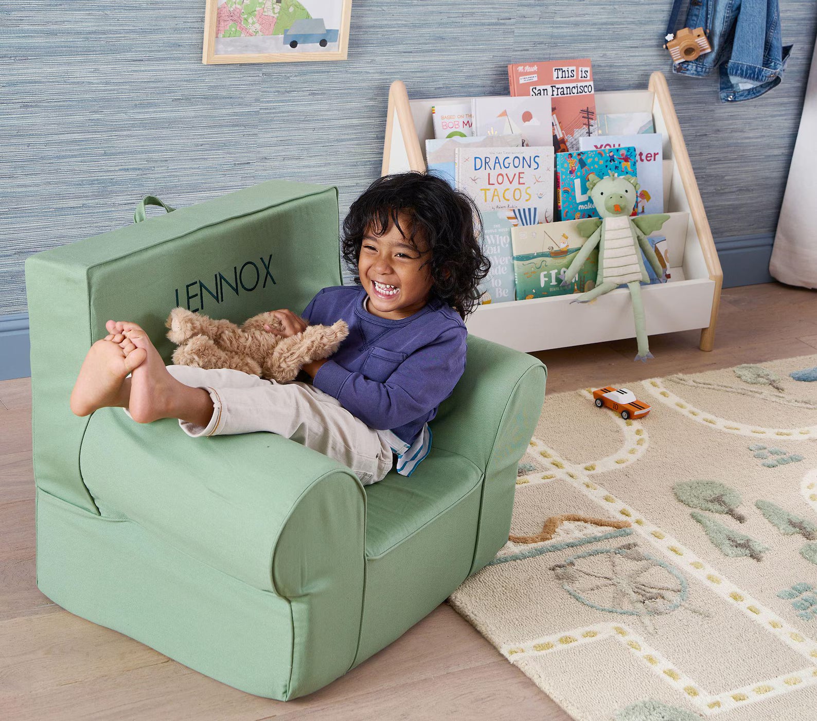 MiniCity hand tufted rug placed behind a child sitting on a mint green chair with a teddy bear, surrounded by books and toys in a cozy kids’ room.