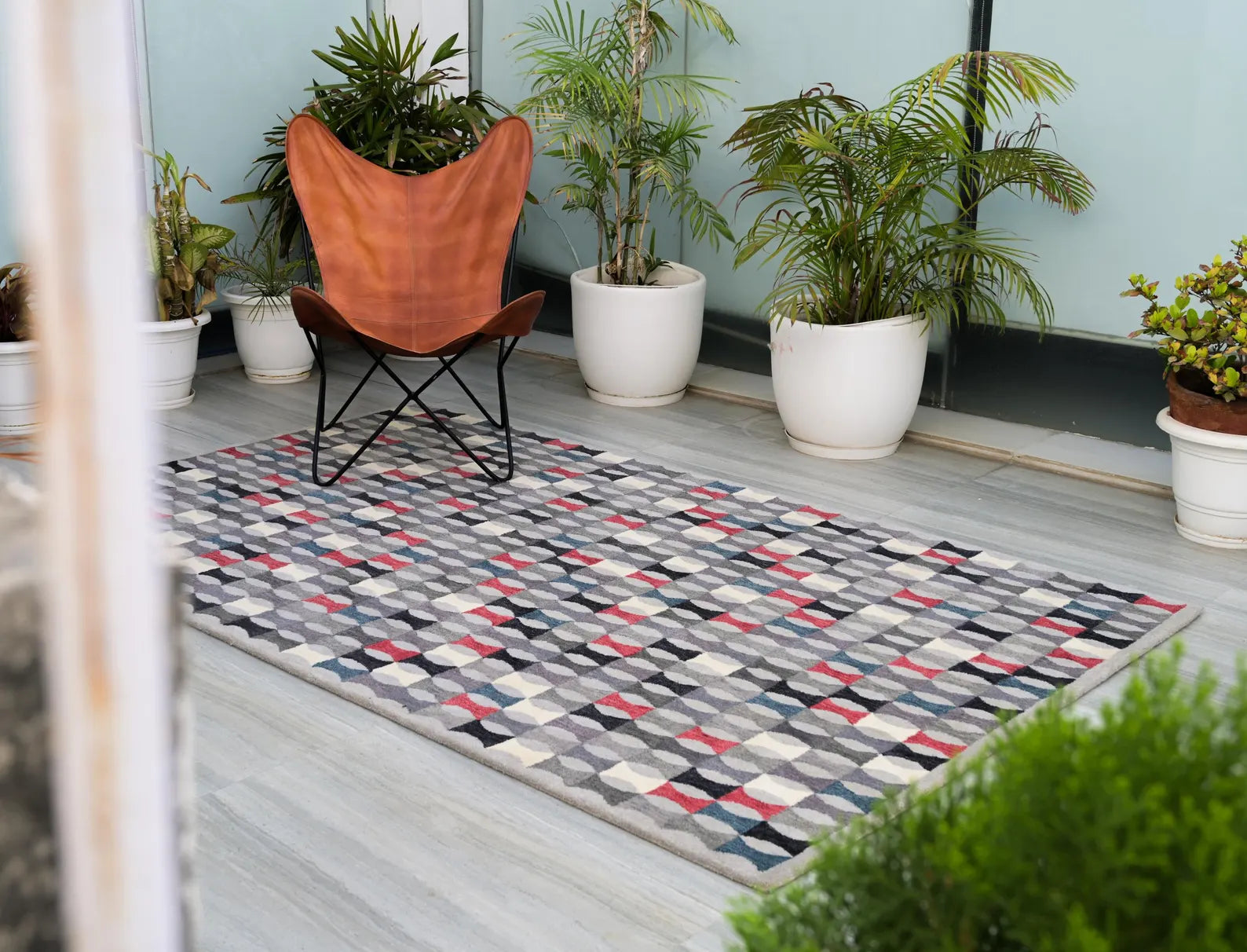 Monotone Matrix hand tufted rug styled in a modern patio setup with plants and neutral decor, featuring a geometric grey and red pattern.