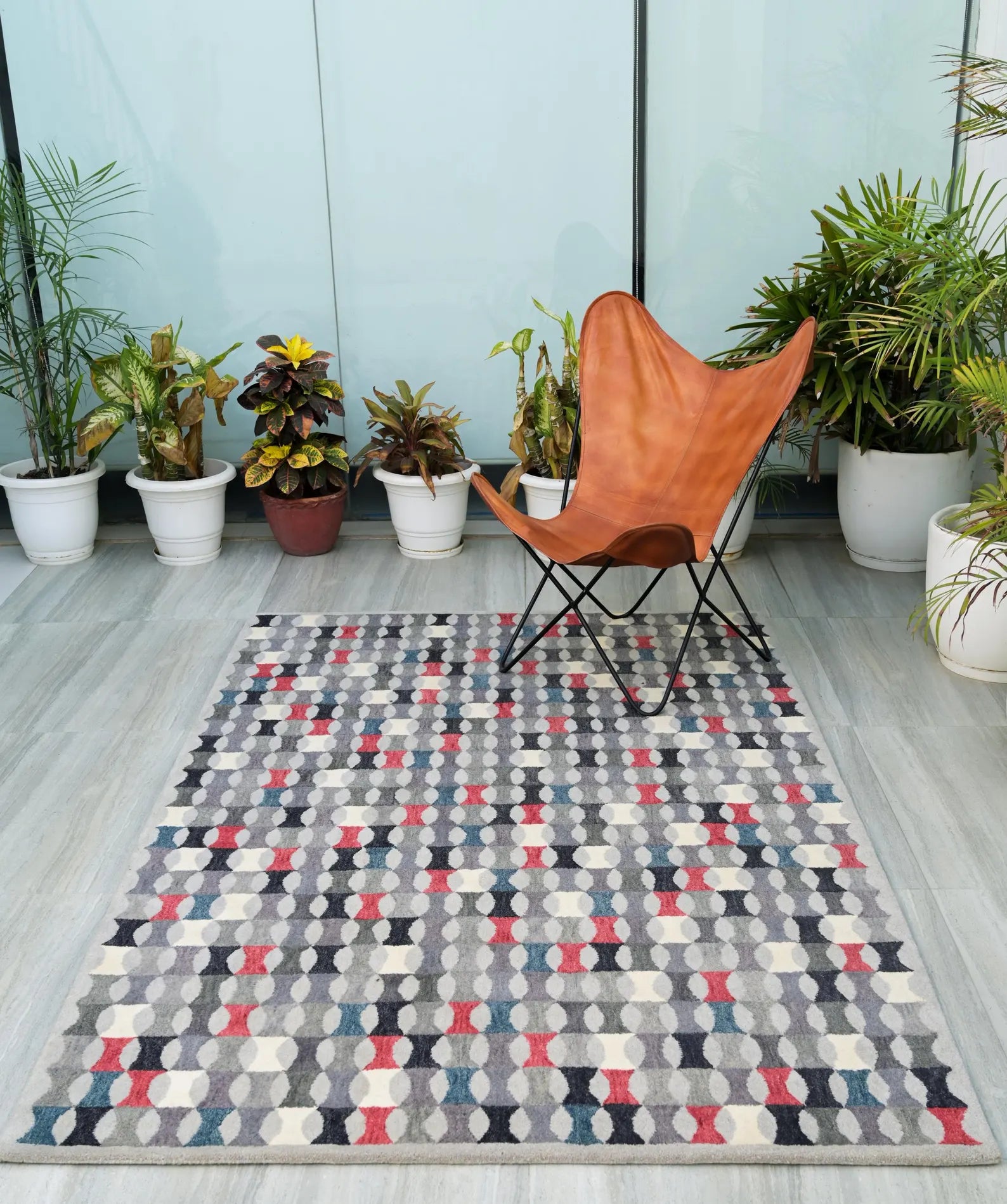 Monotone Matrix hand tufted rug styled with a brown butterfly chair and green potted plants on a modern patio floor, showcasing its geometric red, grey, and white pattern