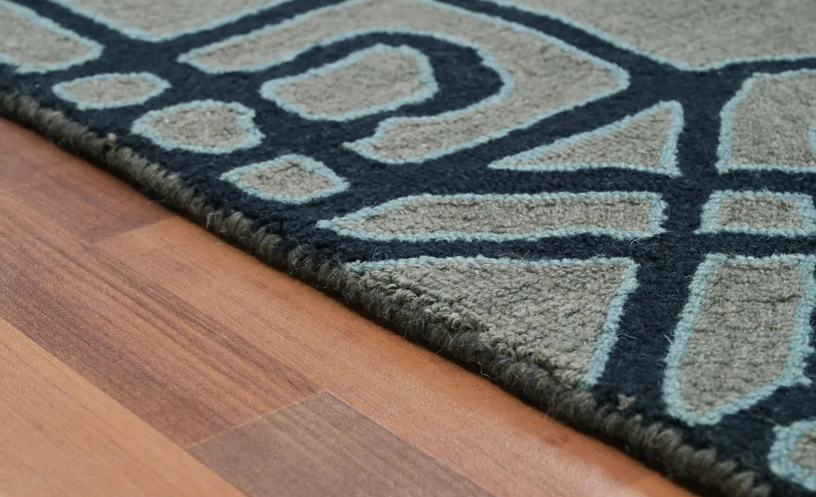 Close-up edge view of Navier hand tufted rug highlighting its navy geometric pattern on a grey base against wooden flooring.