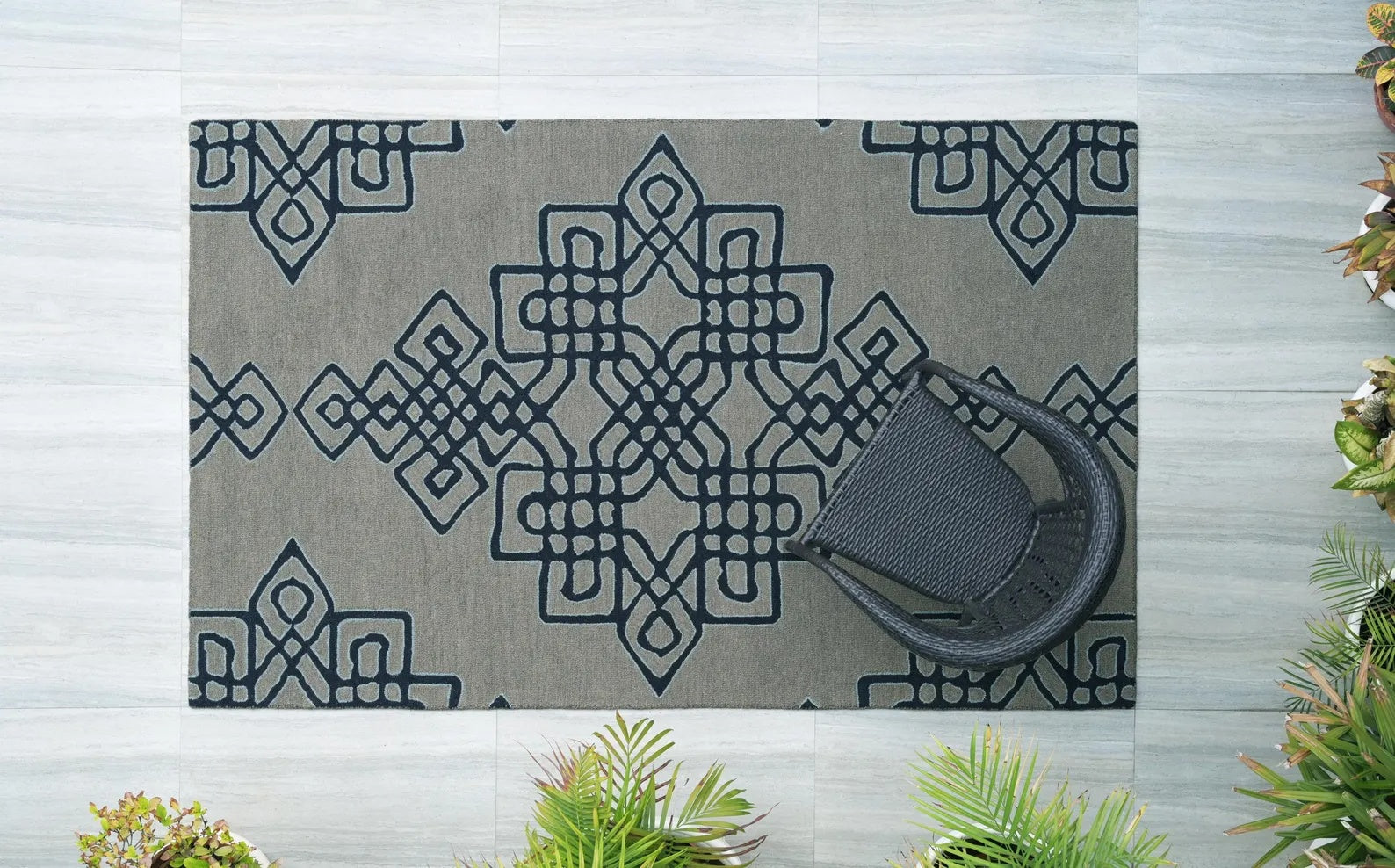 Nexform Rug full view captured from above showing navy geometric pattern on grey base styled with a black chair and indoor plants on light wooden flooring