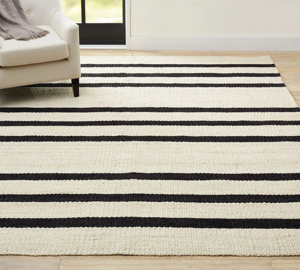 Noirpath Rug styled in a bright living room with black horizontal stripes on an ivory base, placed on a wooden floor beside a sofa.