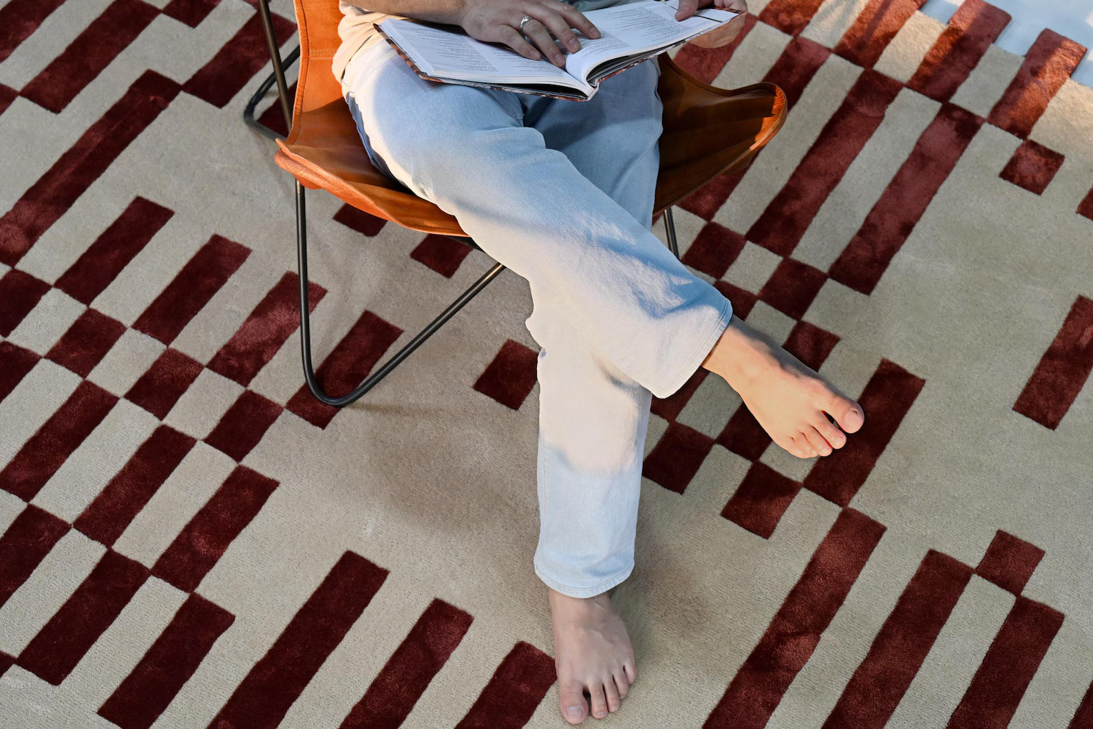 Person sitting barefoot on the Pixelated Rug, showing the texture and bold red grid design.
