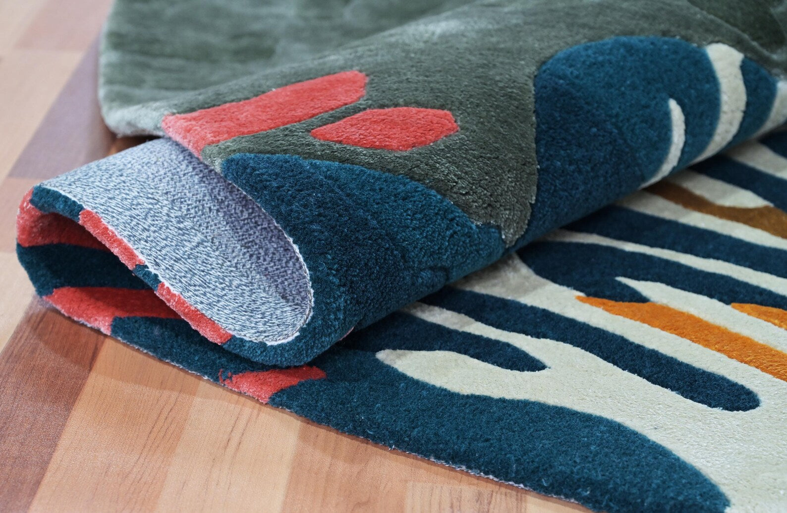 Seaform Hand tufted Rug fold overlap showing layered marine-inspired colors in deep blue, green, coral, and ivory tones with soft tufted texture on wooden flooring