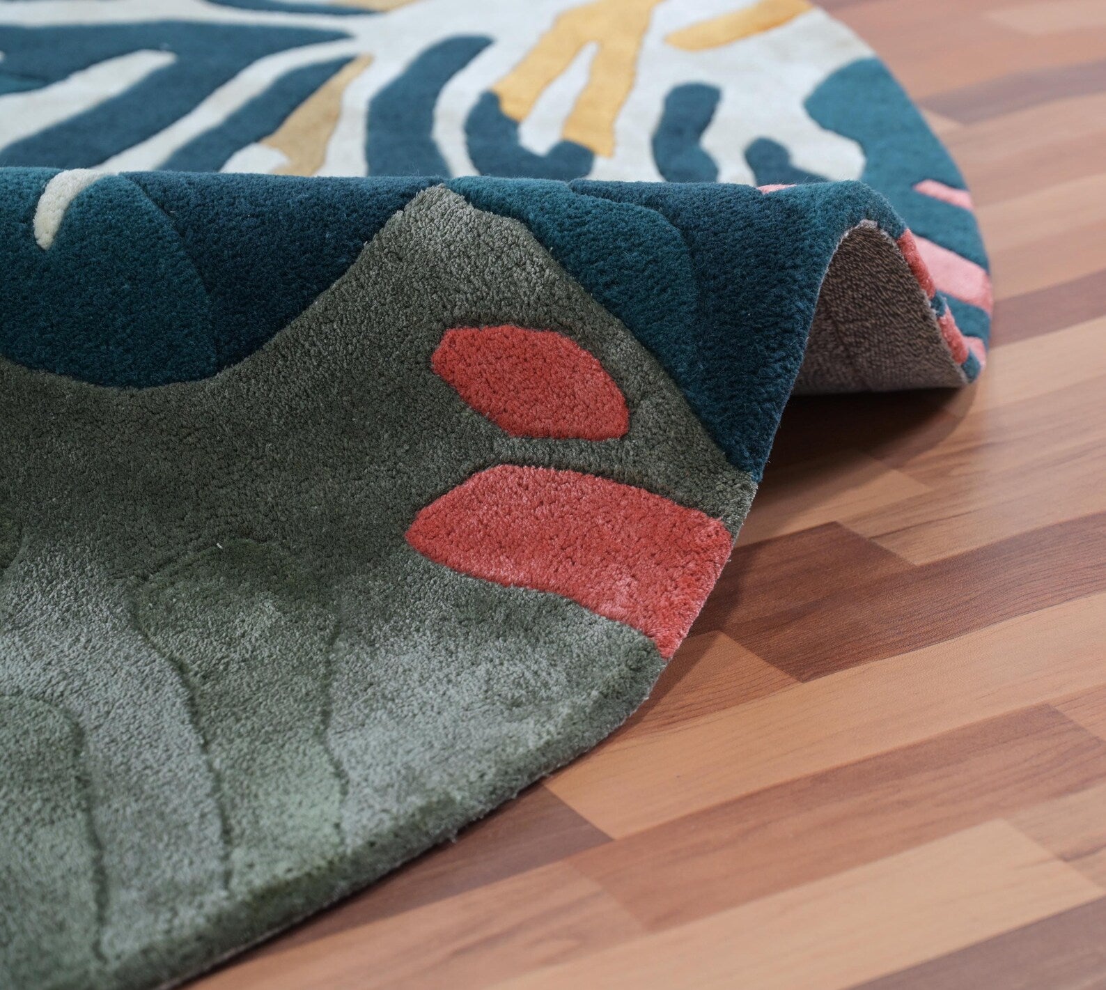 Seaform Rug edge fold showing ocean-inspired color transitions in blue, green, and coral shades with soft hand finished detailing on wooden flooring