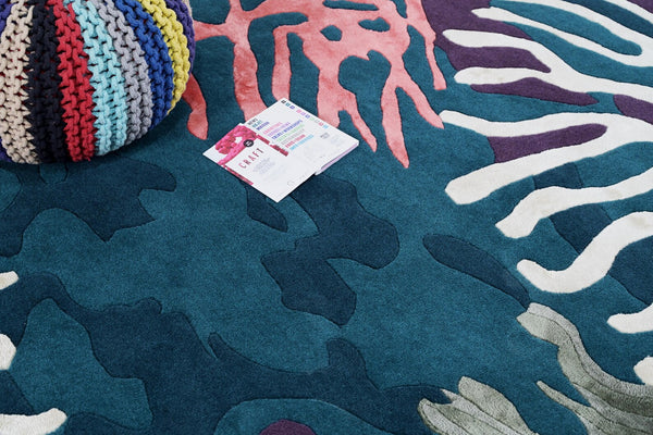 Seaform Rug lifestyle view highlighting artisan hand tufted finish with vibrant marine tones styled alongside a colorful pouf and magazine on a wooden floor