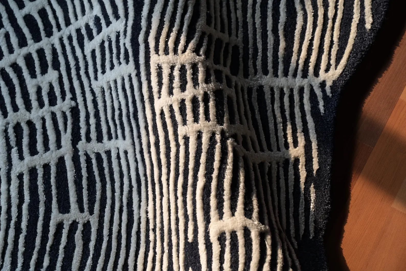 Close-up detail of Sequoia Rug highlighting its soft hand-tufted texture, white line pattern, and dark wool base illuminated by natural light on a wooden floor.
