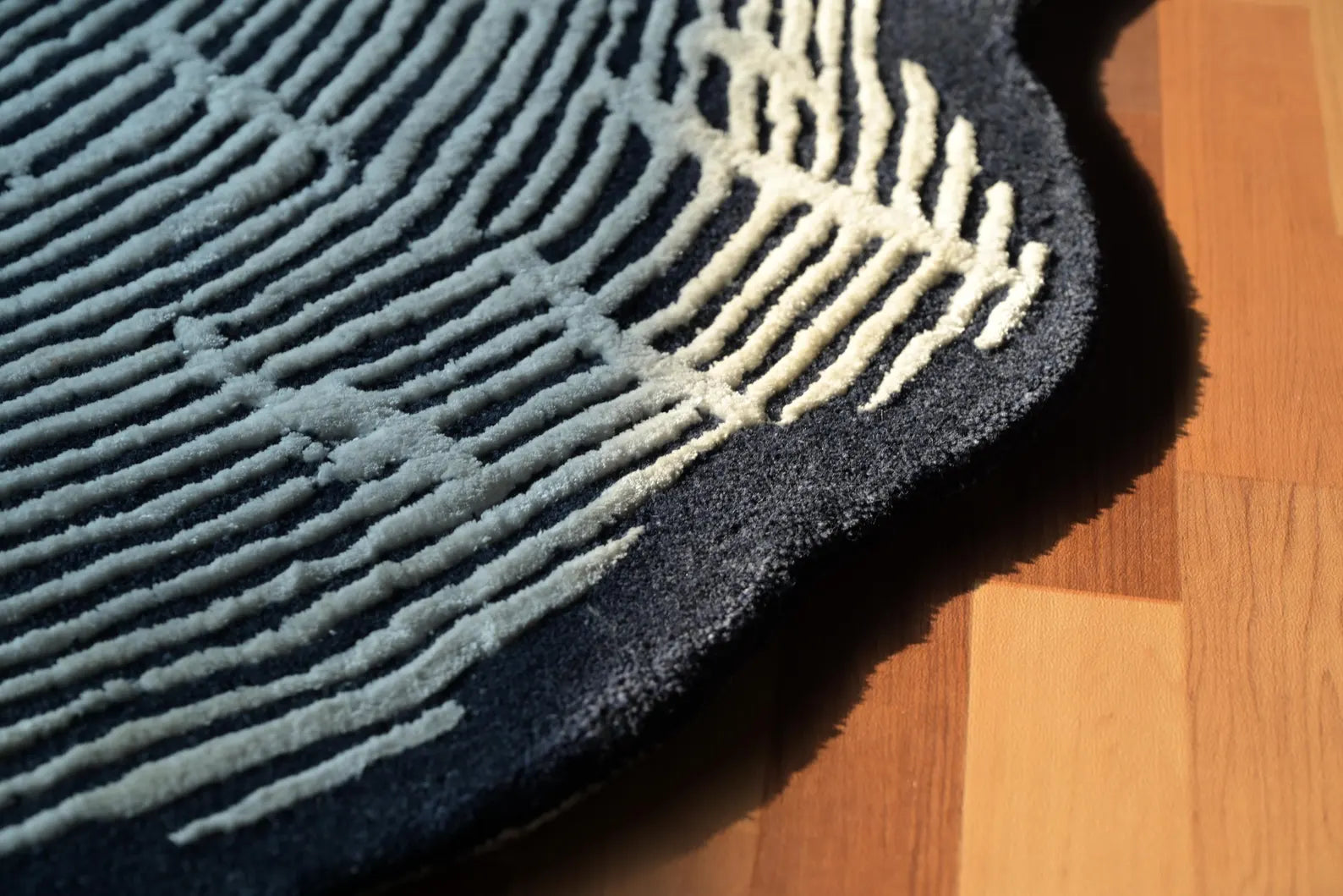 Sequoia Rug edge detail under natural light showing raised white linear tufting on a dark charcoal base with softly curved organic borders.