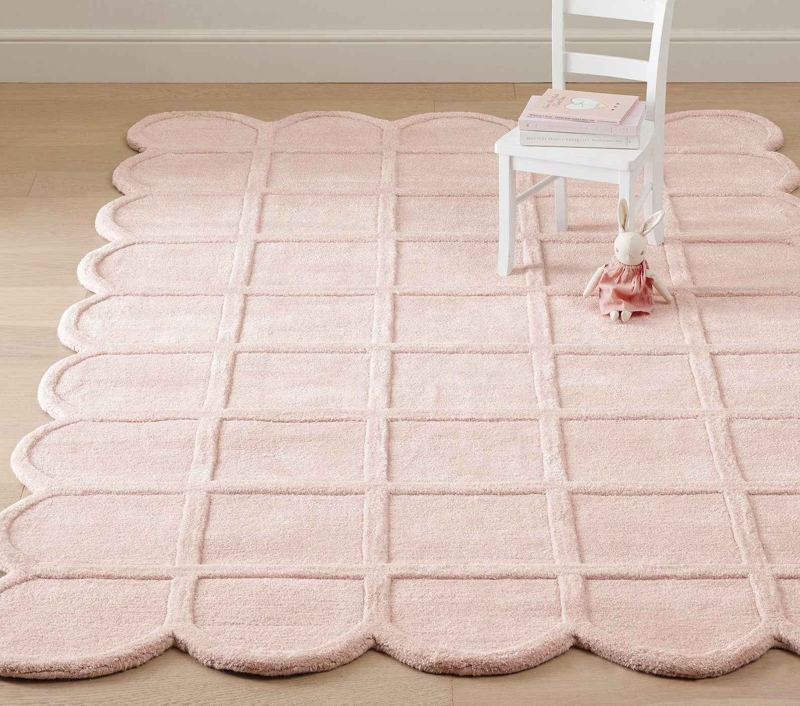 Seraphine Blush Rug styled in a kids’ room with a white chair and soft toy, highlighting its scalloped edges, gentle blush tone, and plush hand-tufted grid texture.