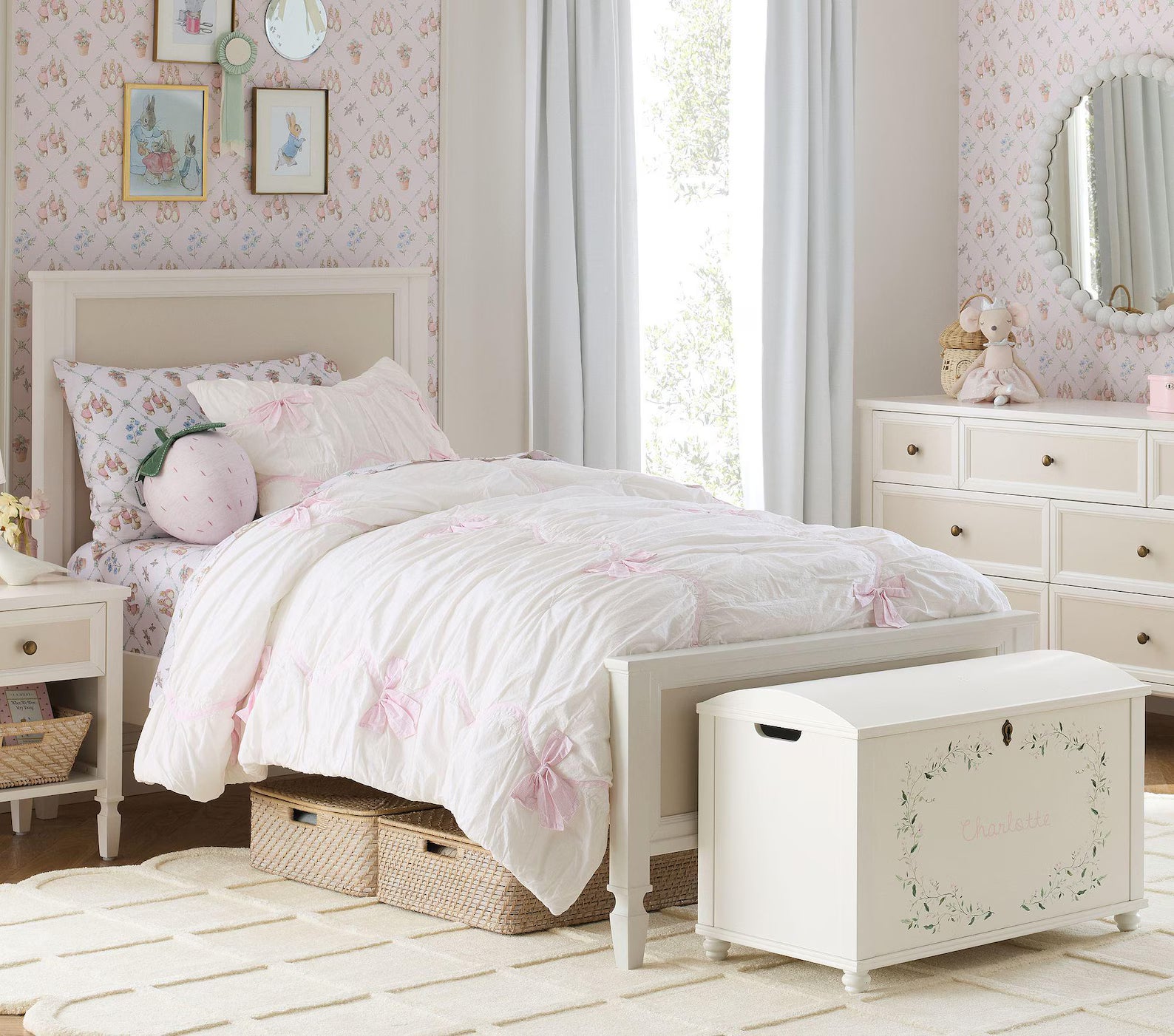 Seraphine Petal hand tufted rug placed in a pastel kids’ bedroom beneath a white bed and storage chest, showcasing its scalloped edge detailing and soft blush hue from a wide interior view angle.