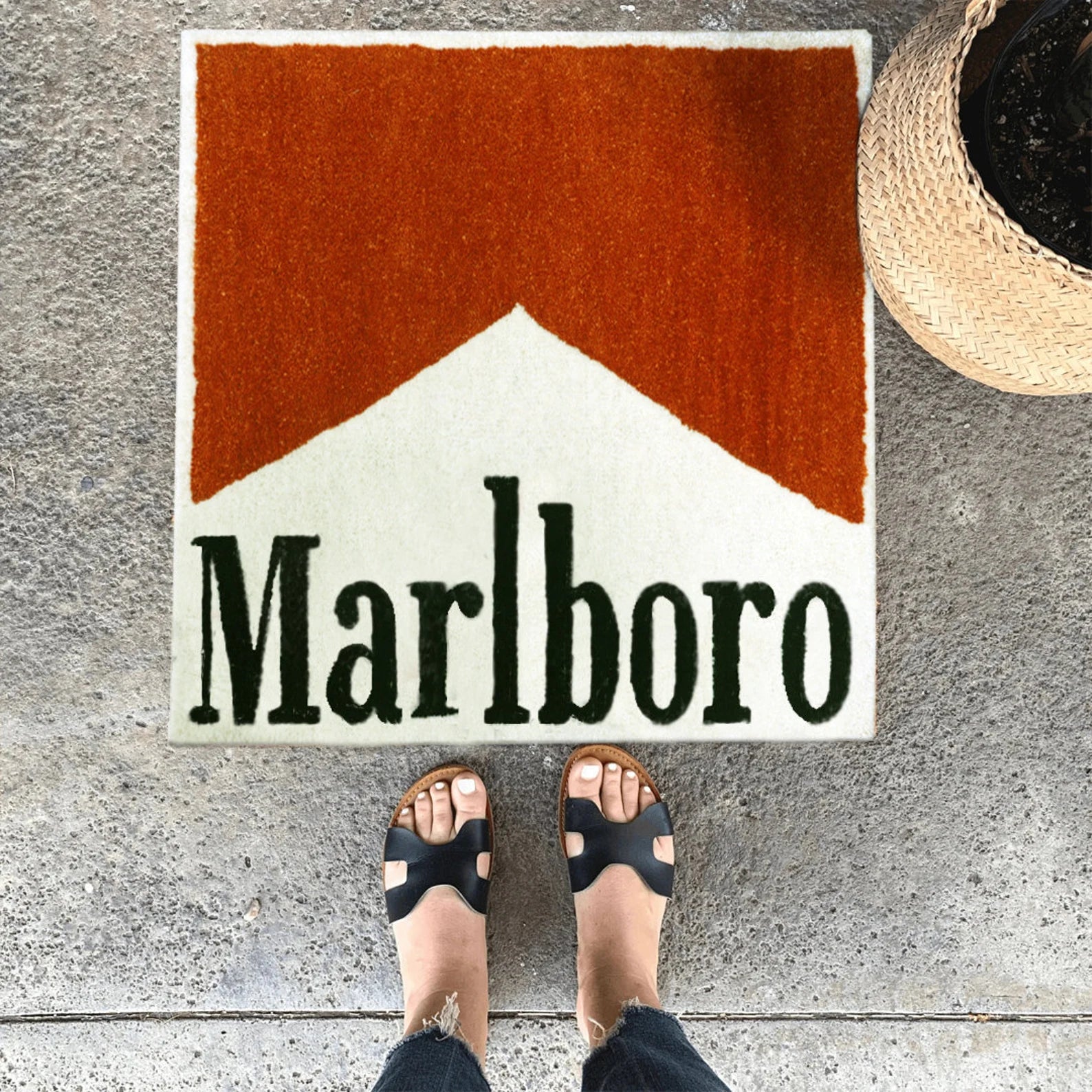 Top angle styled view of Marlboro Doormat placed on concrete floor showing bold red and white design with black lettering