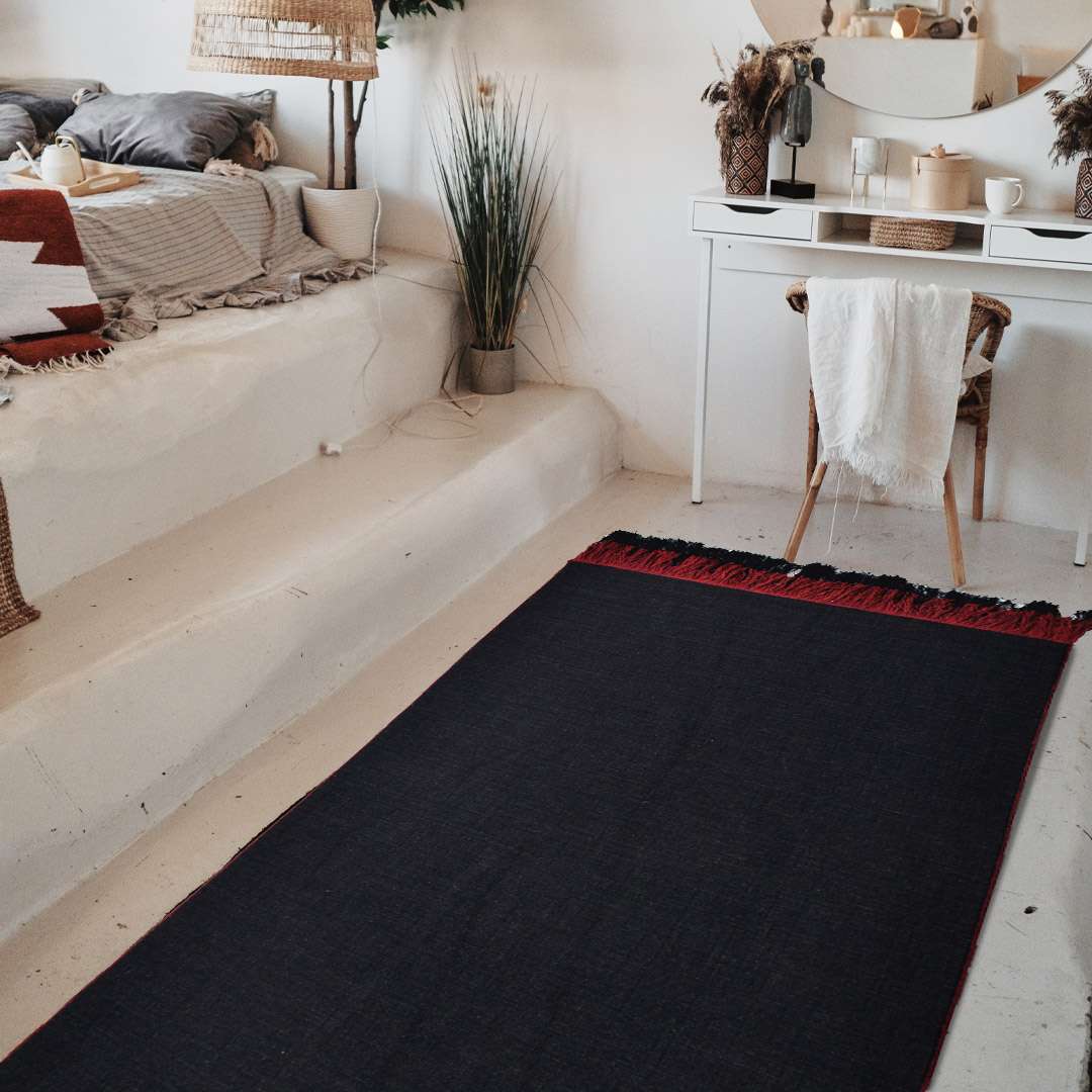 Top angle view of Auskin Luxury Black Rug placed in a minimal living room with red tasseled edges and soft black texture