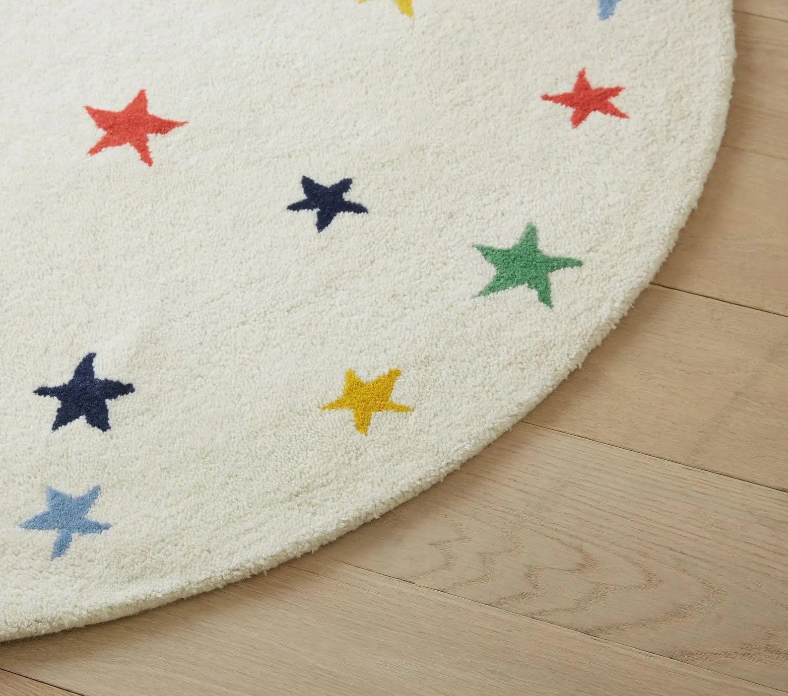 Corner view of Twinkle Rug Round featuring vibrant multicolored stars on a soft ivory wool surface, showcasing precise hand-tufted detailing and smooth round edges for a refined, playful look.