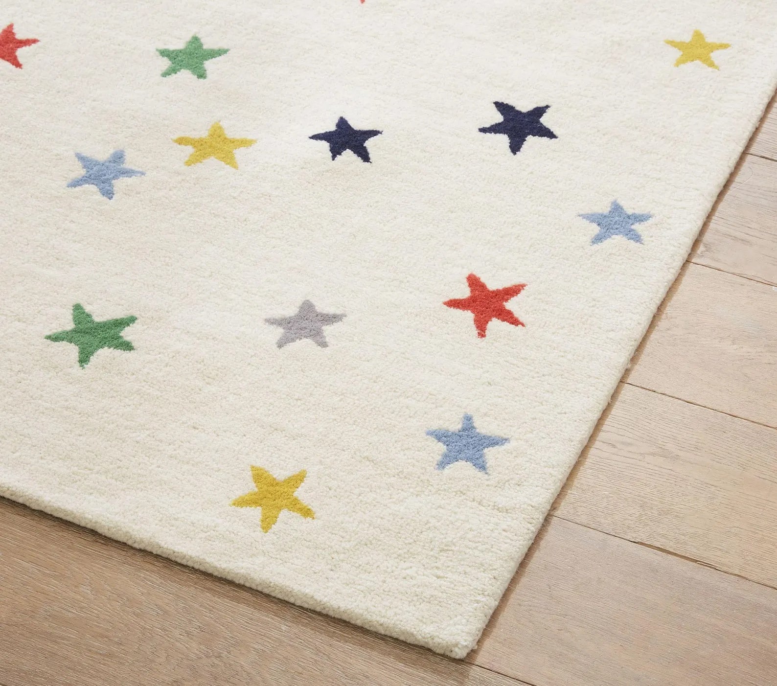 Corner view of Twinkle hand tufted rug featuring multicolored stars on a creamy wool surface, showcasing clean edges and soft hand-tufted texture for a playful finish. 