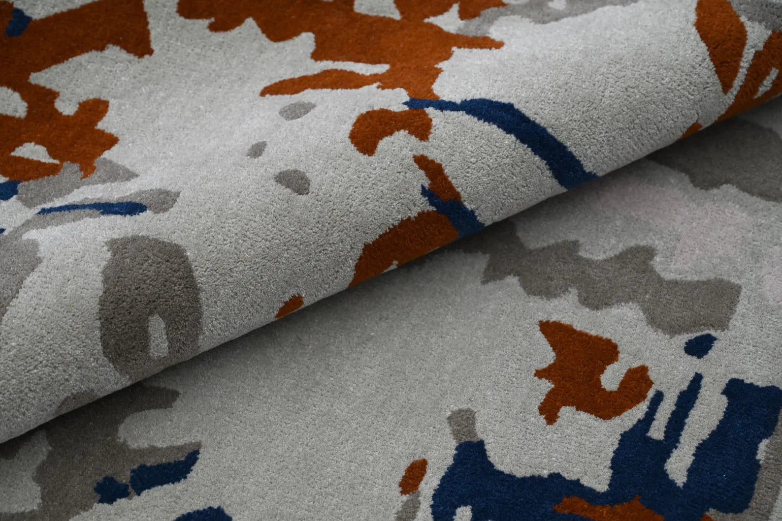 Folded layer of Vortex Distressed Rug highlighting its abstract pattern with blue, rust, and gray tones over a smooth wool surface
