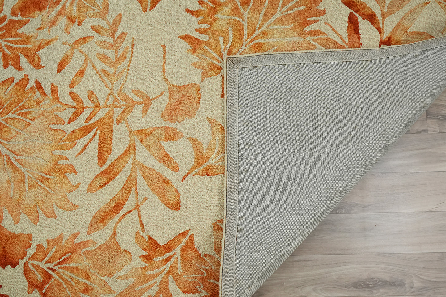 Autumna hand tufted wool rug showing a folded corner with backing visible and the leaf design continuing across the surface