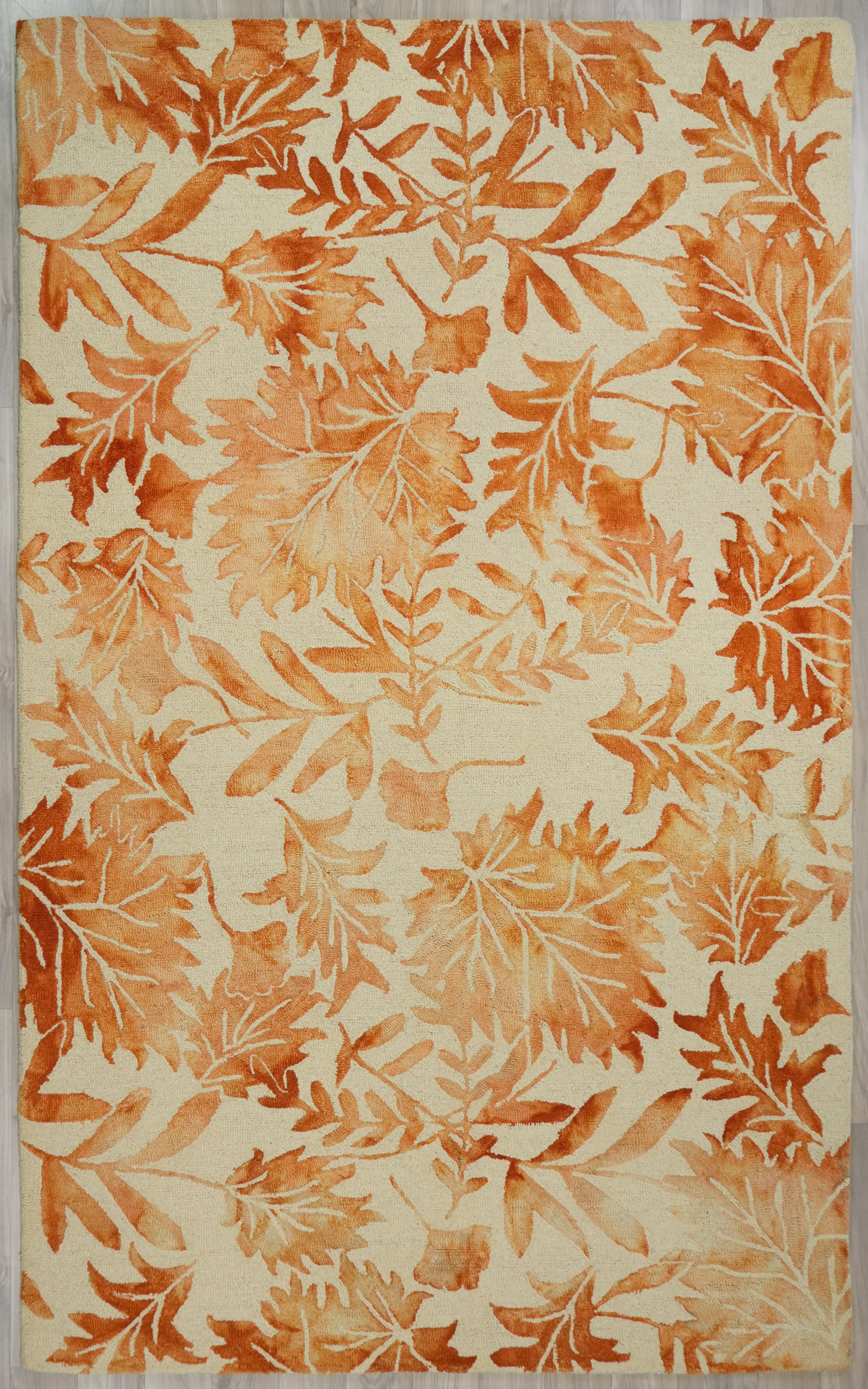 Autumna hand tufted wool rug shown in full view featuring an all over leaf pattern in warm orange tones on a light neutral background