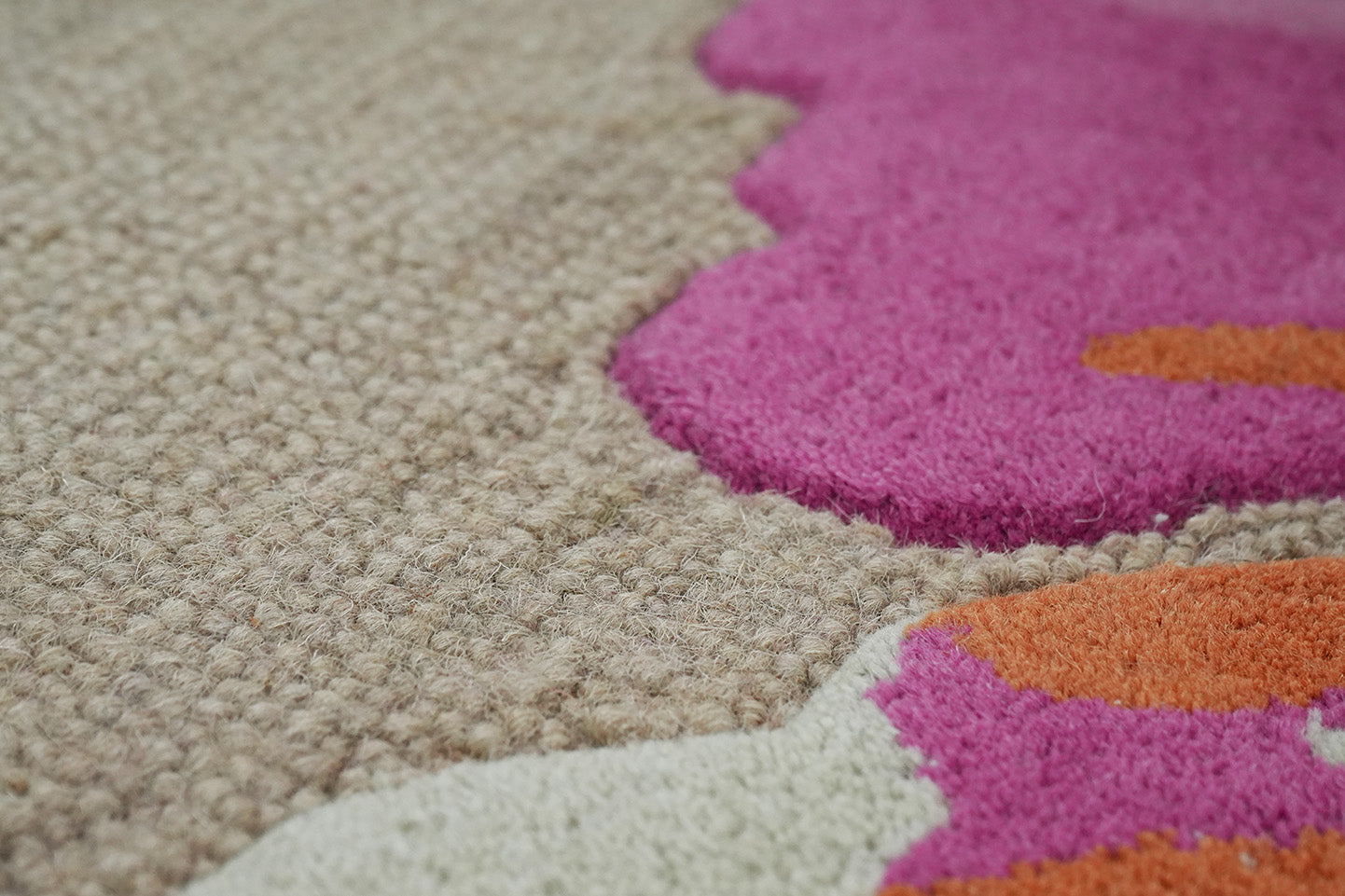 Bloomscape Floral Wool Rug made from 100 % New Zealand wool with hand tufted construction shown in close up highlighting textured pile and layered floral shapes in pink, coral, and warm tones on a neutral base