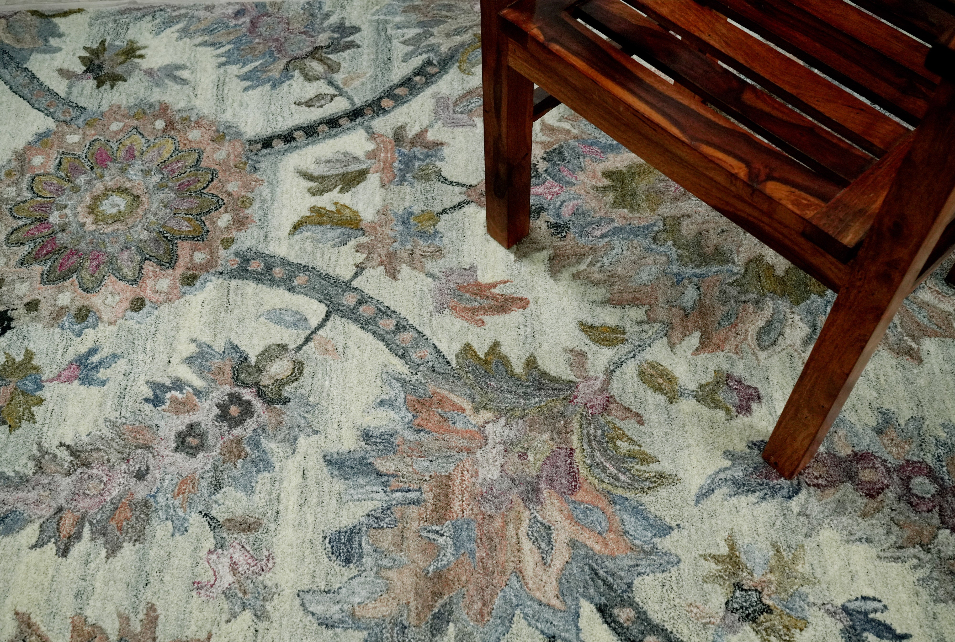 Briarwood hand tufted rug in a heritage floral design placed under a wooden bench showing ivory base with blush sage and dusty blue accents