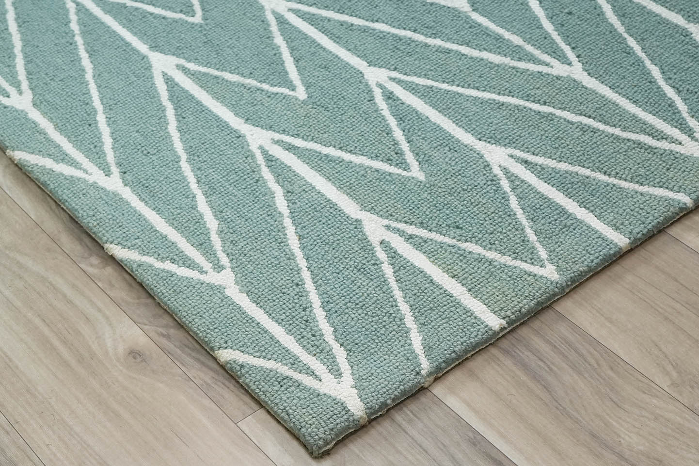 Angled view of Chevron Drift hand tufted rug highlighting the sage green base and ivory chevron lines