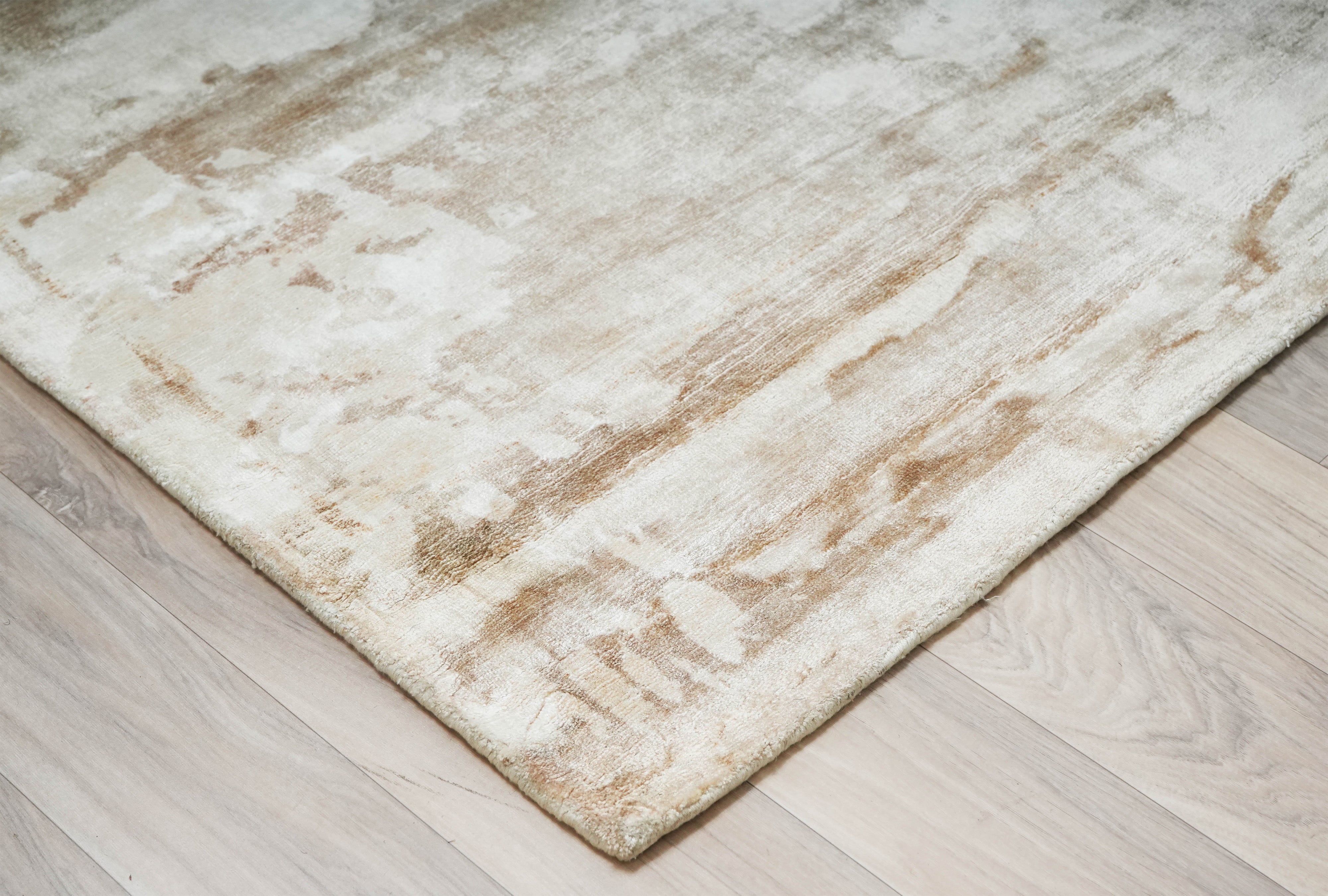 Corner detail of Clouded Earth beige wool hand tufted rug on light wooden floor.