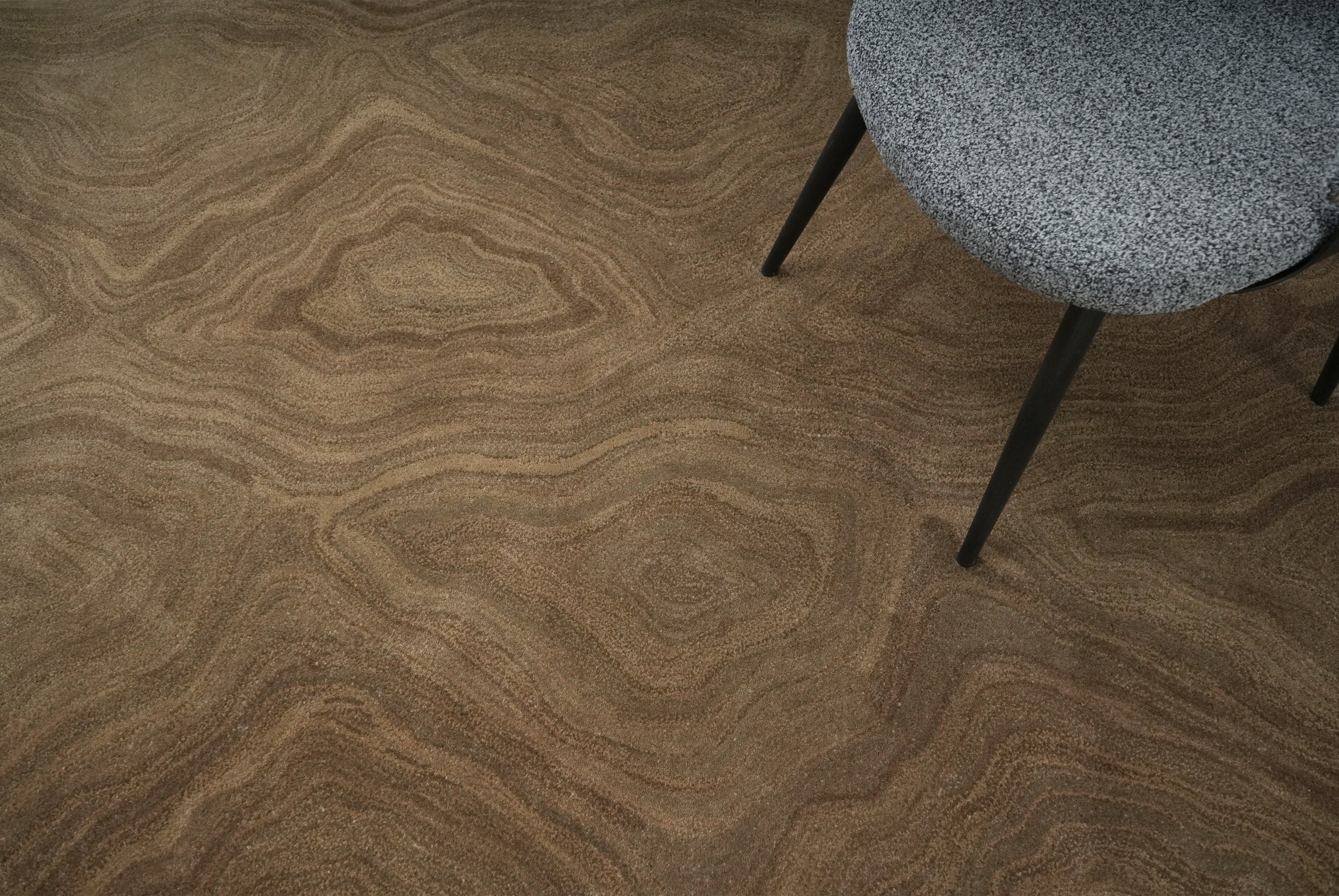 Earthen hand tufted wool rug detail under chair showing organic texture in warm brown tones