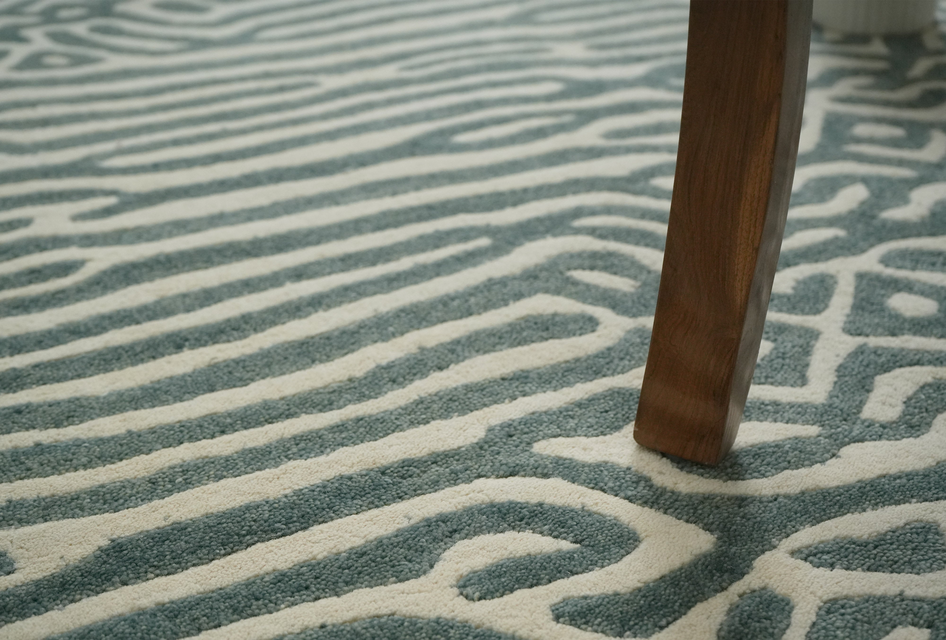Glyph hand tufted wool rug detail under table leg showing textured pattern in sage green and ivory