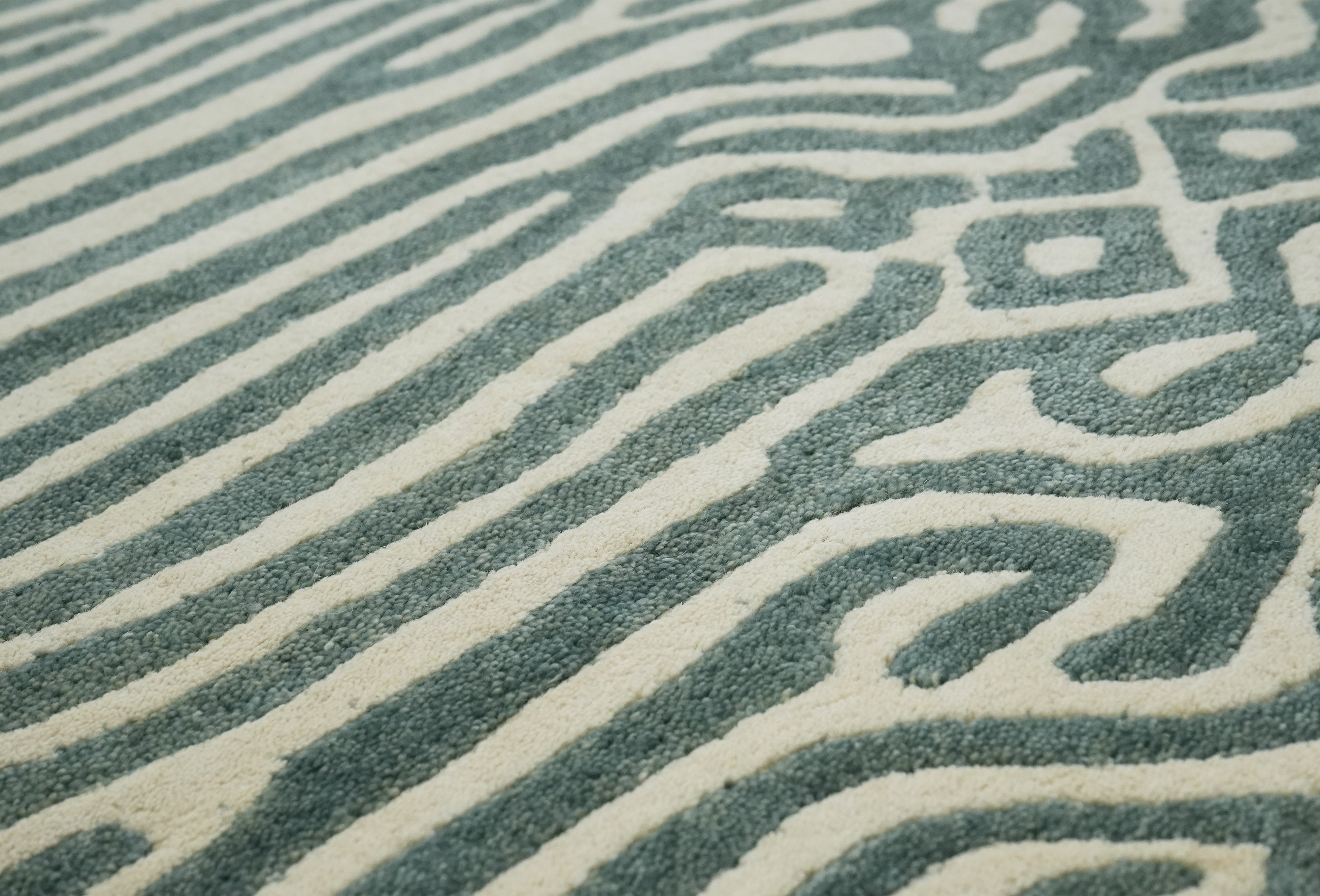 Low angle close up of Glyph hand tufted wool rug showing textured pattern in sage green and ivory