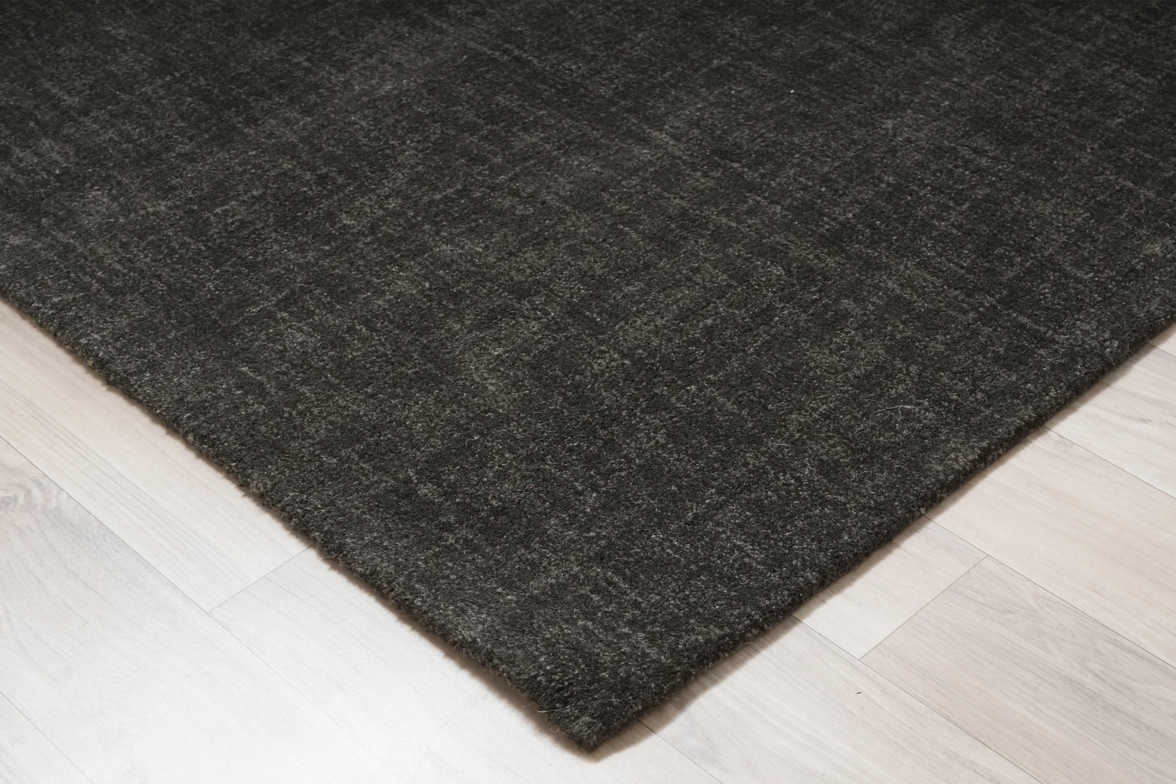 Corner detail of Graphite Shadow charcoal wool hand tufted rug on light wooden floor.