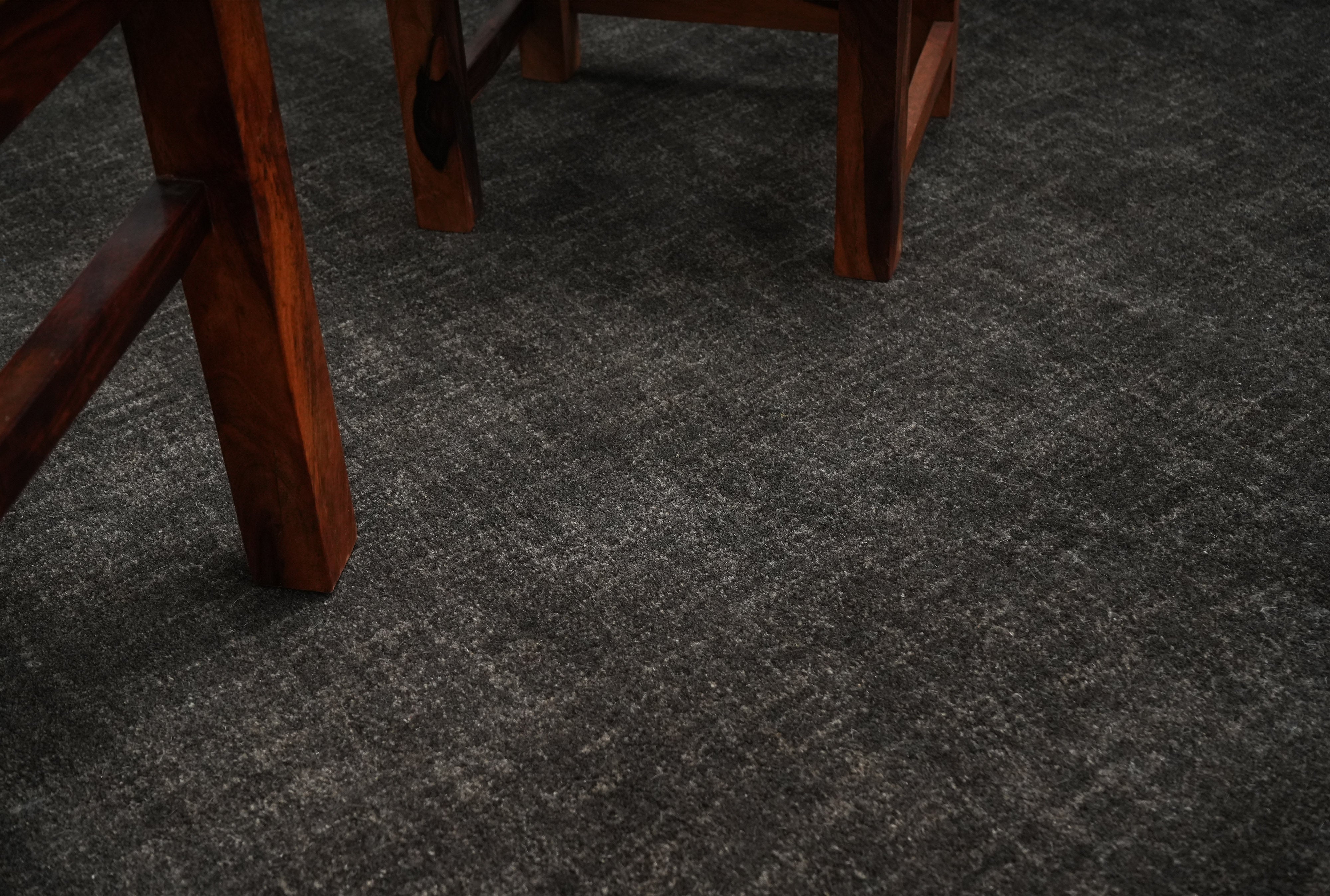 Graphite Shadow charcoal wool hand tufted rug beneath wooden furniture legs.