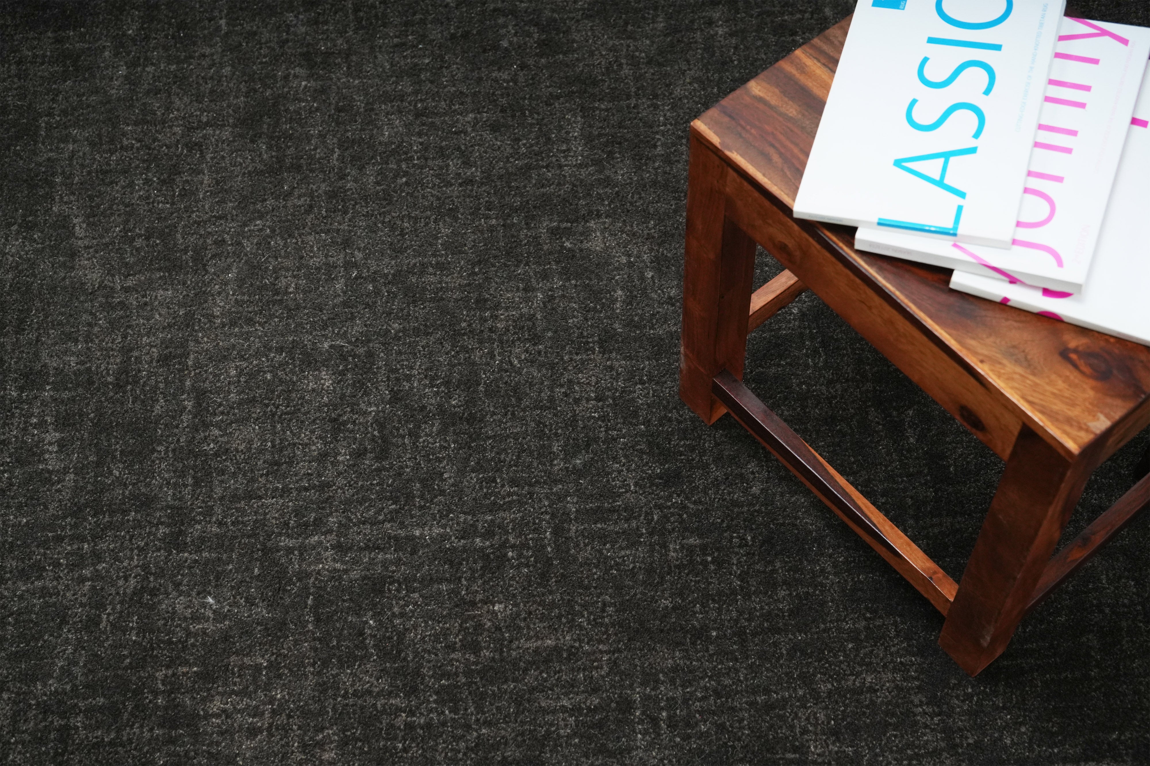 Graphite Shadow charcoal wool hand tufted rug styled with wooden stool and books.