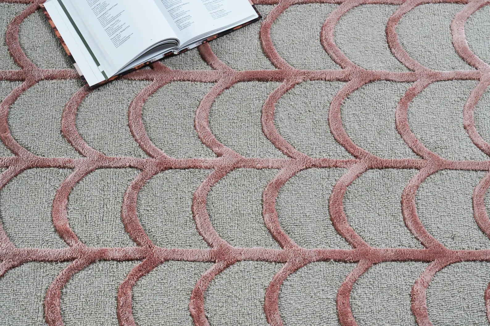 Hand tufted Geometric Scallop hand tufted rug in a styled detail view with an open book placed on top, highlighting its raised scallop pattern and textured surface.