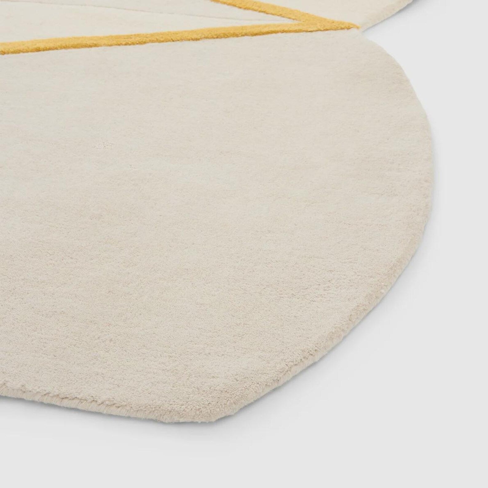 Hand tufted Rayform hand tufted rug in a corner view showing its smooth ivory surface with a minimal golden accent line and soft sculptural shape.