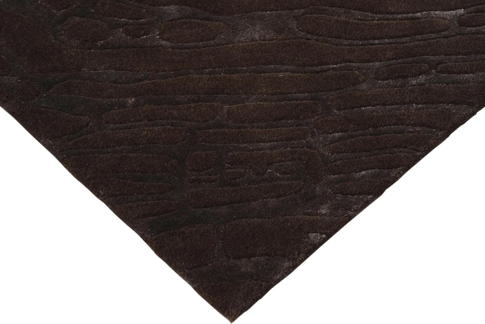 Neatly finished corner of the hand tufted Fossil Ember rug with visible fossil like carving lines.