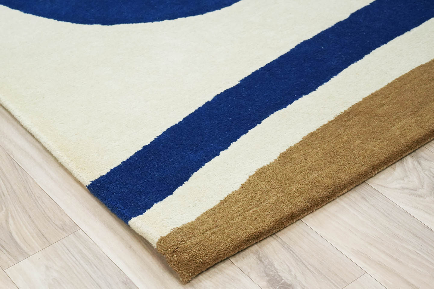 Border detail of Interlinked Circle hand tufted rug showing ivory base with deep blue and earthy brown accents